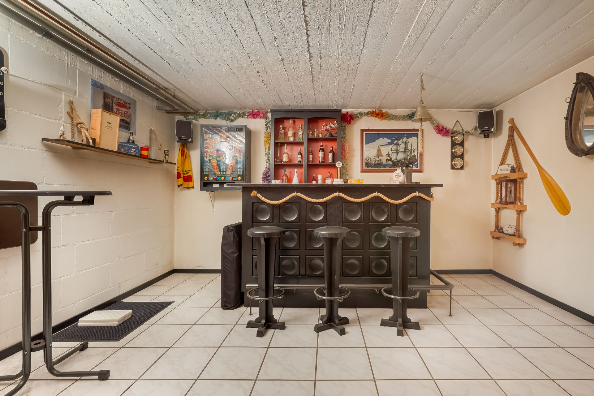 Kellerraum mit Hausbar, drei Barhockern und Wanddekorationen im maritimen Stil.