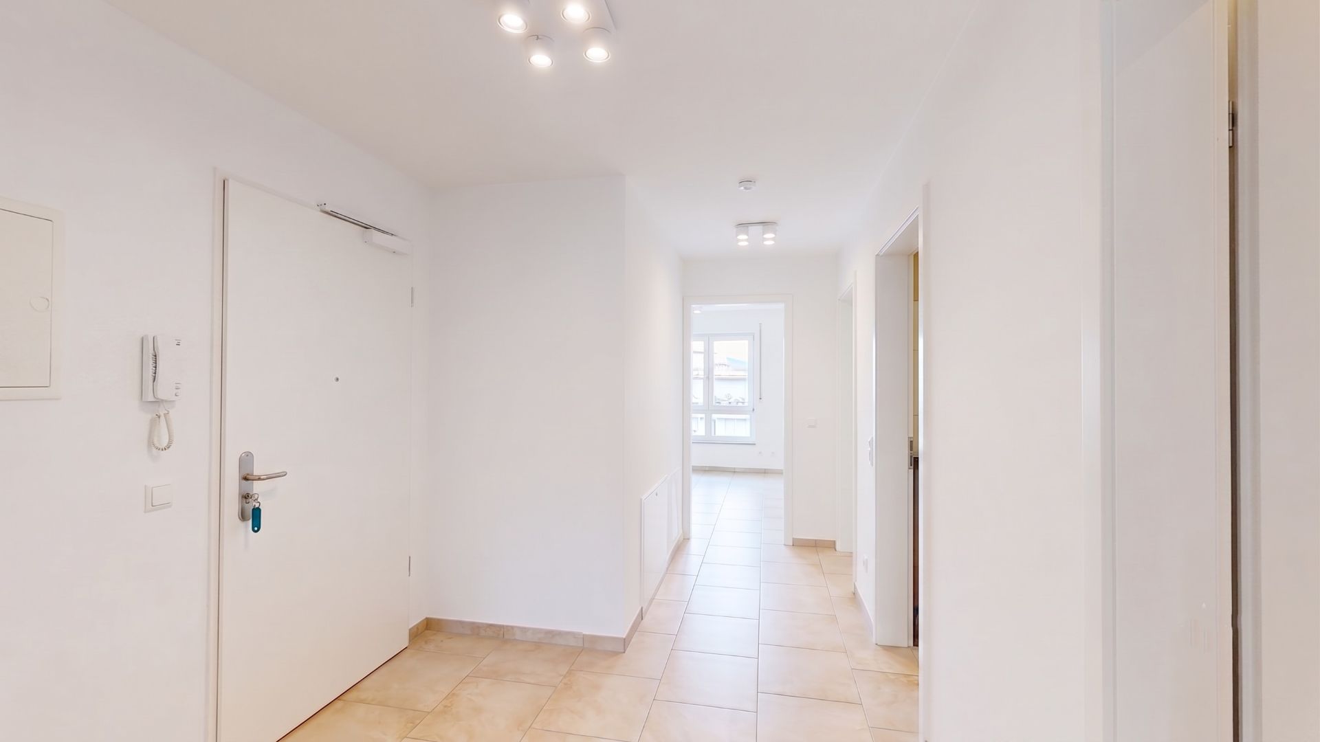 Heller Flur mit Fliesenboden, weißen Wänden und mehreren Türen in einer Wohnung.