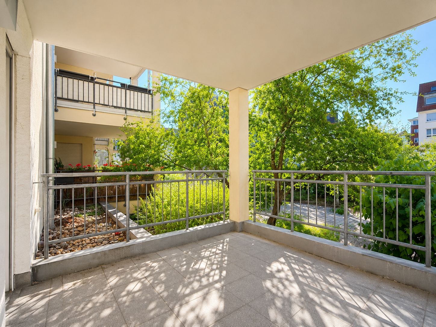 Überdachter Balkon mit Metallgeländer, Blick auf Garten und angrenzende Wohngebäude.