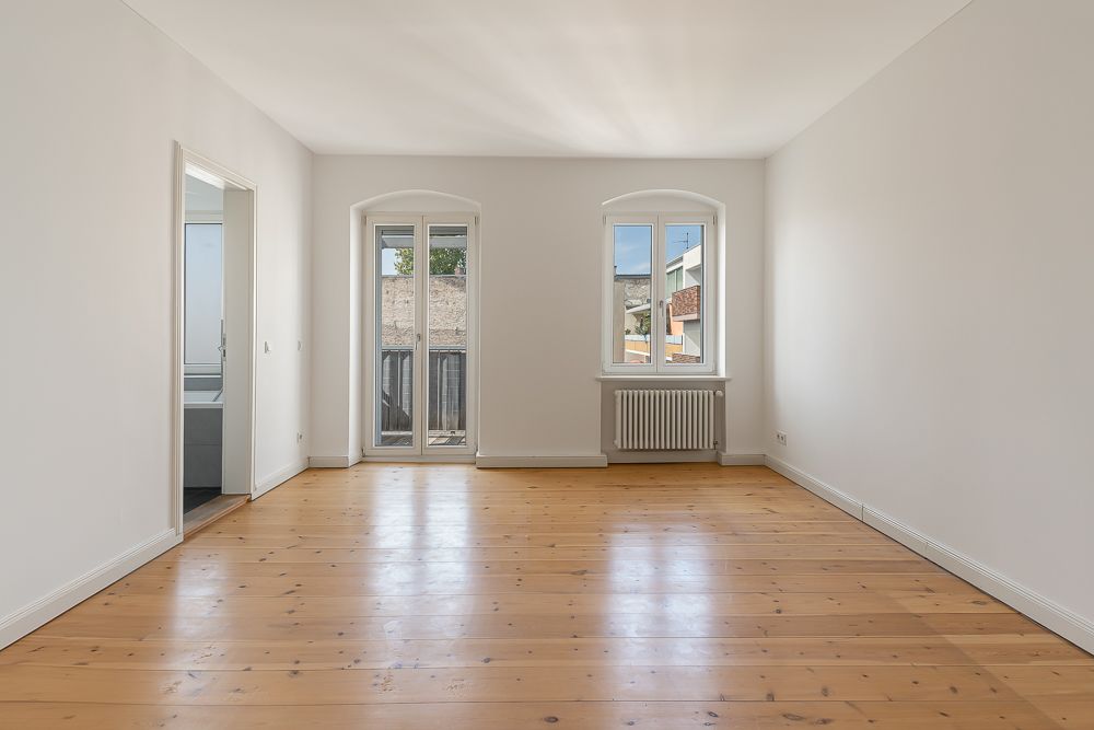 Leerer Raum mit Holzboden, zwei Fenstern und weiß gestrichenen Wänden.