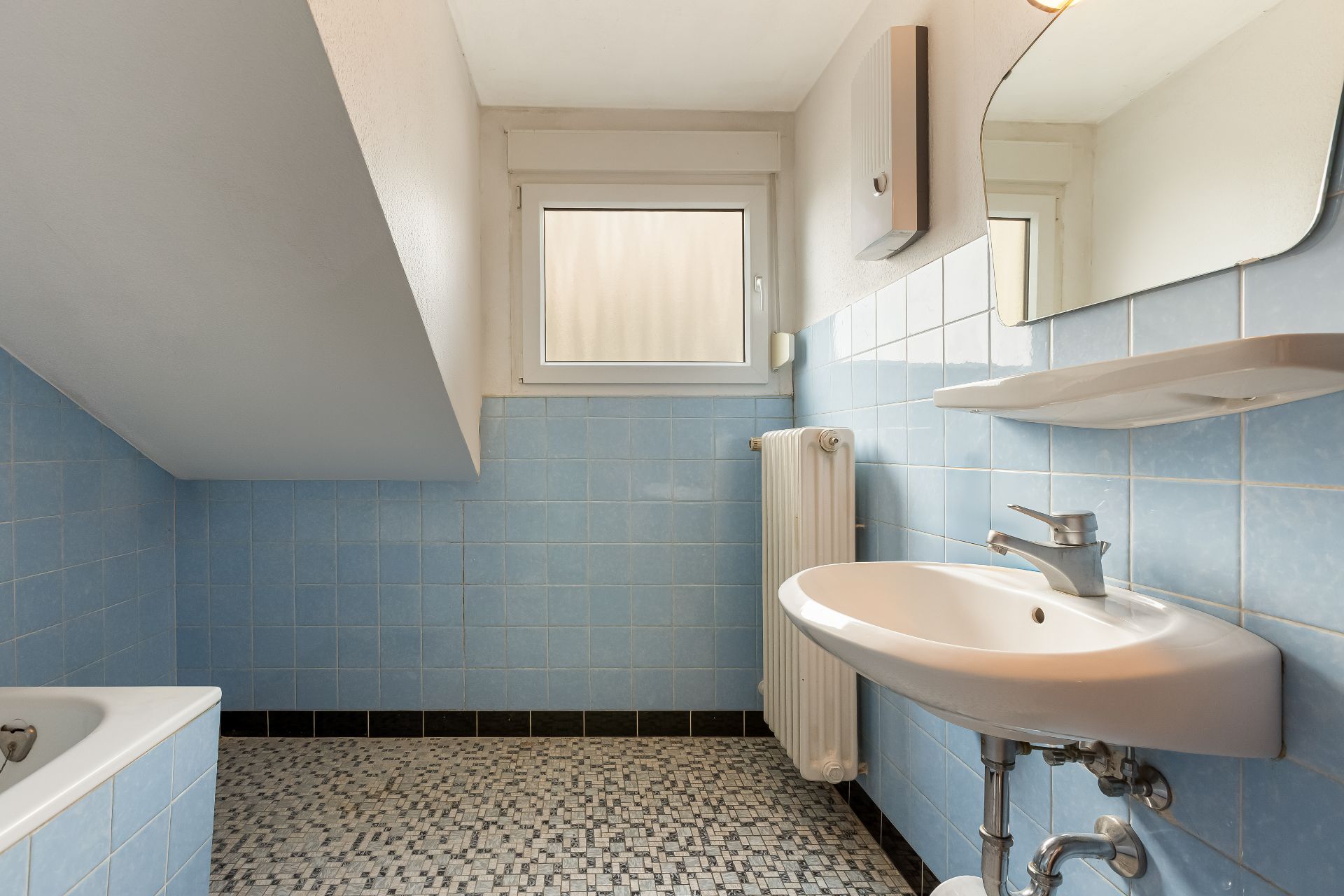 Helles Badezimmer mit blau gefliesten Wänden, Waschbecken, Spiegel und Fenster.