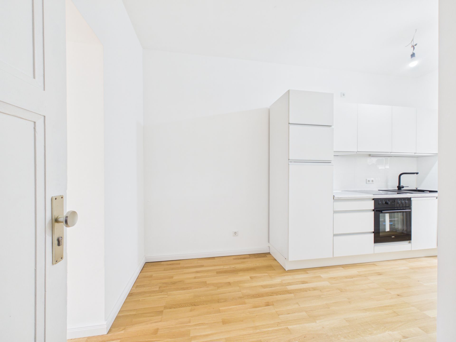 Helle Einbauküche mit weißen Schränken und Holzfußboden in einem leeren Raum.