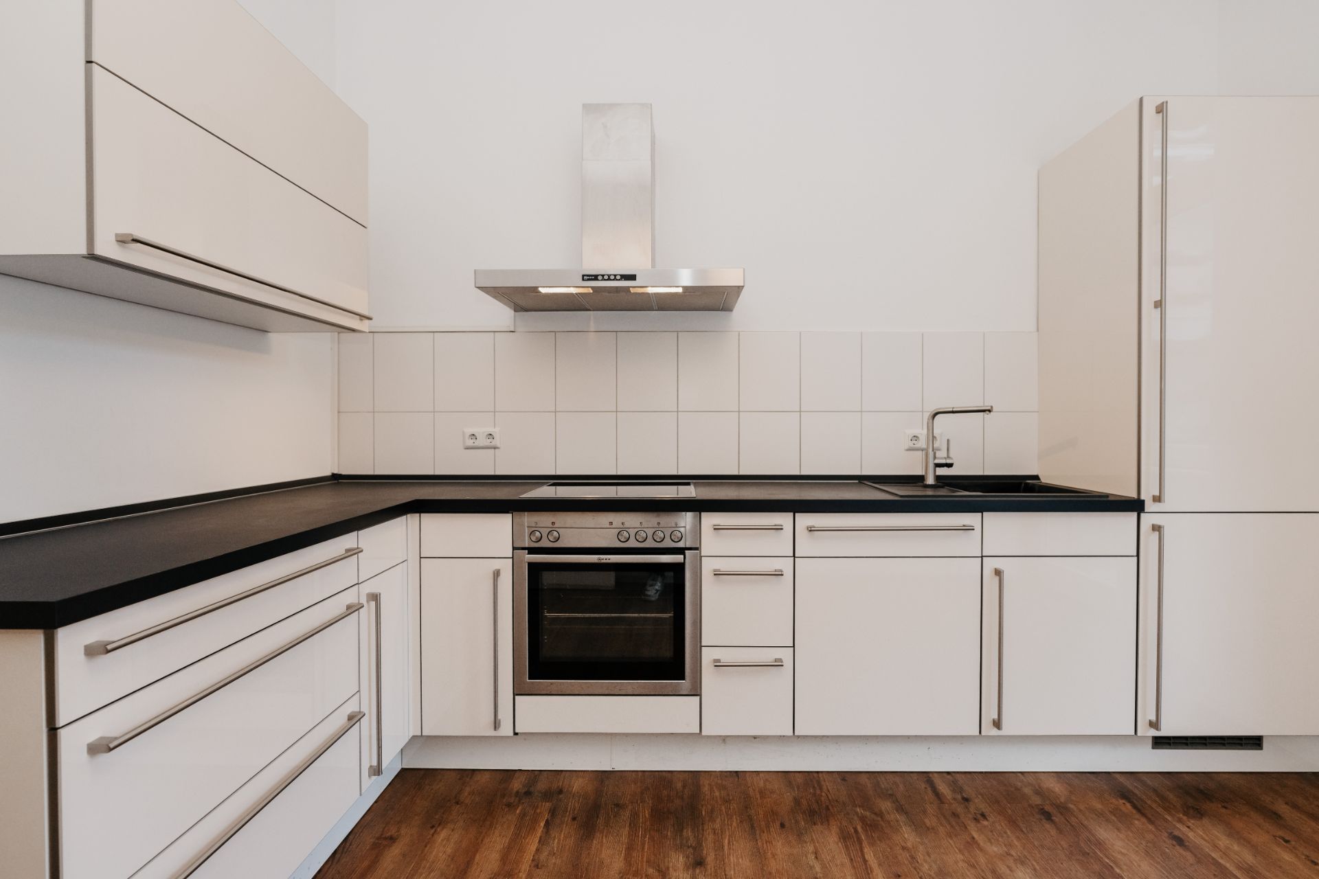 Moderne Einbauküche mit weißen Schränken, Backofen, Herd und Spüle auf Holzfußboden.