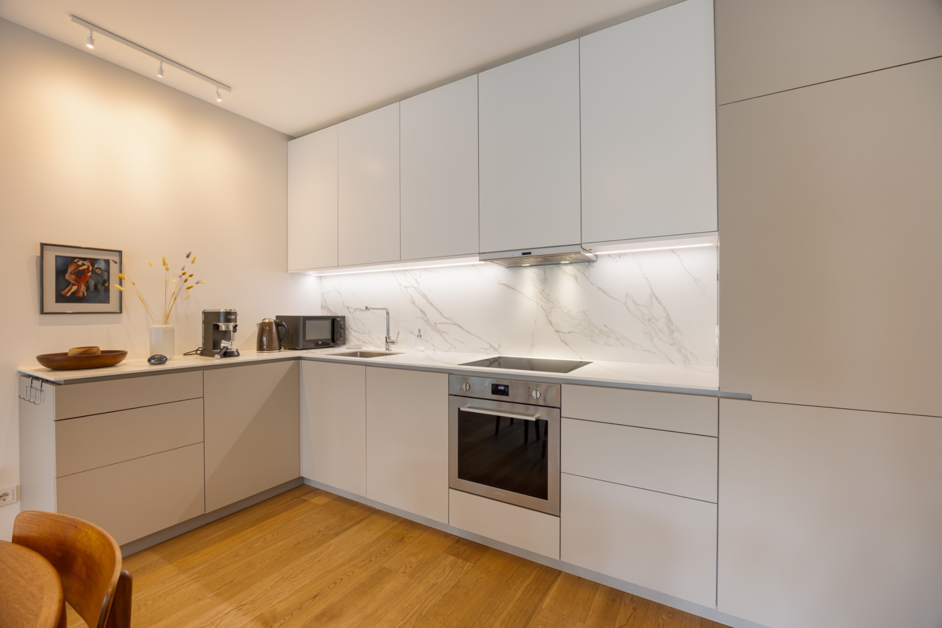 Moderne Einbauküche mit weißen Schränken, Elektrogeräten und Holzfußboden.