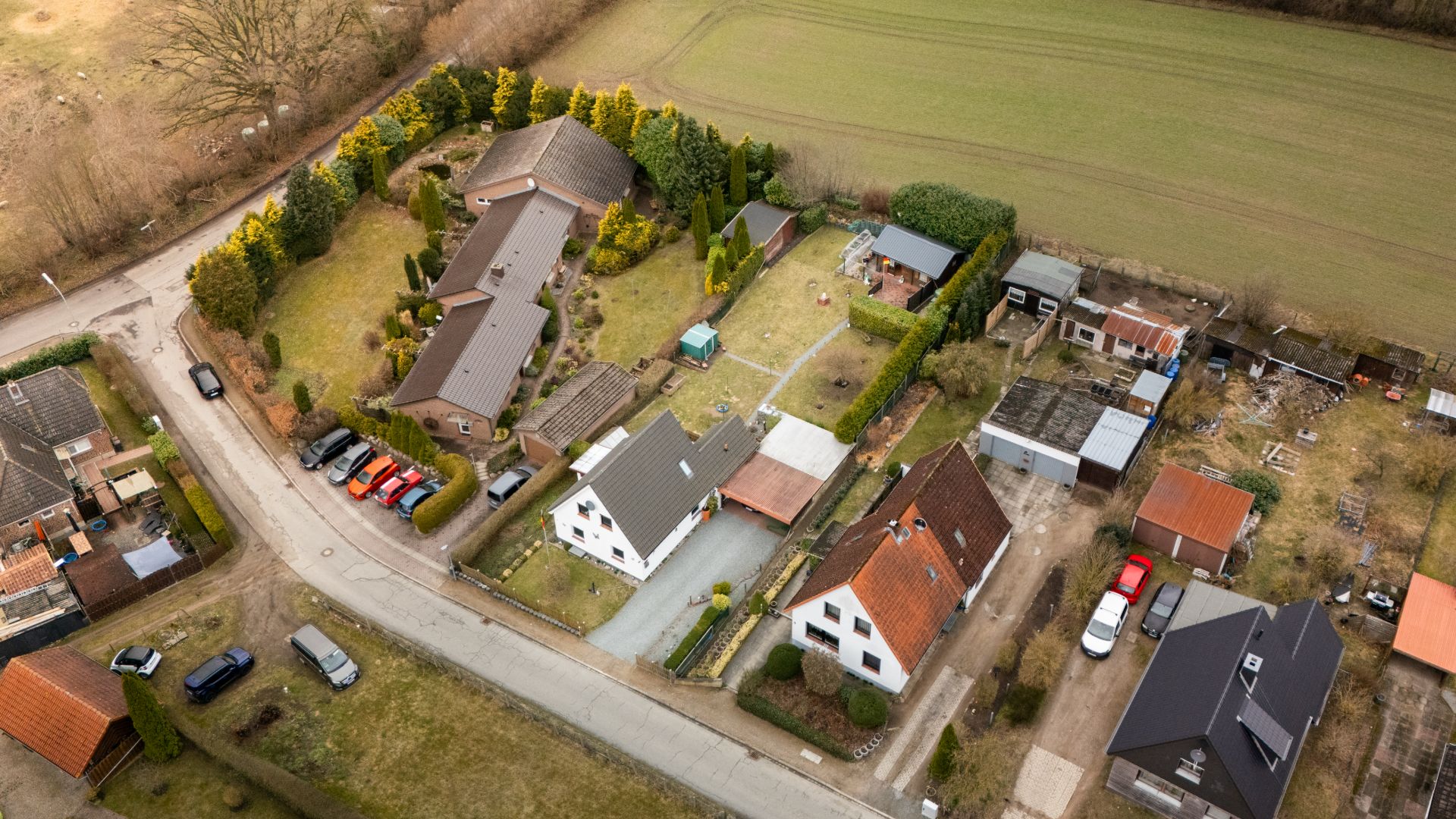 Luftaufnahme von Wohnhäusern mit Gärten und parkenden Autos in einer ländlichen Gegend.