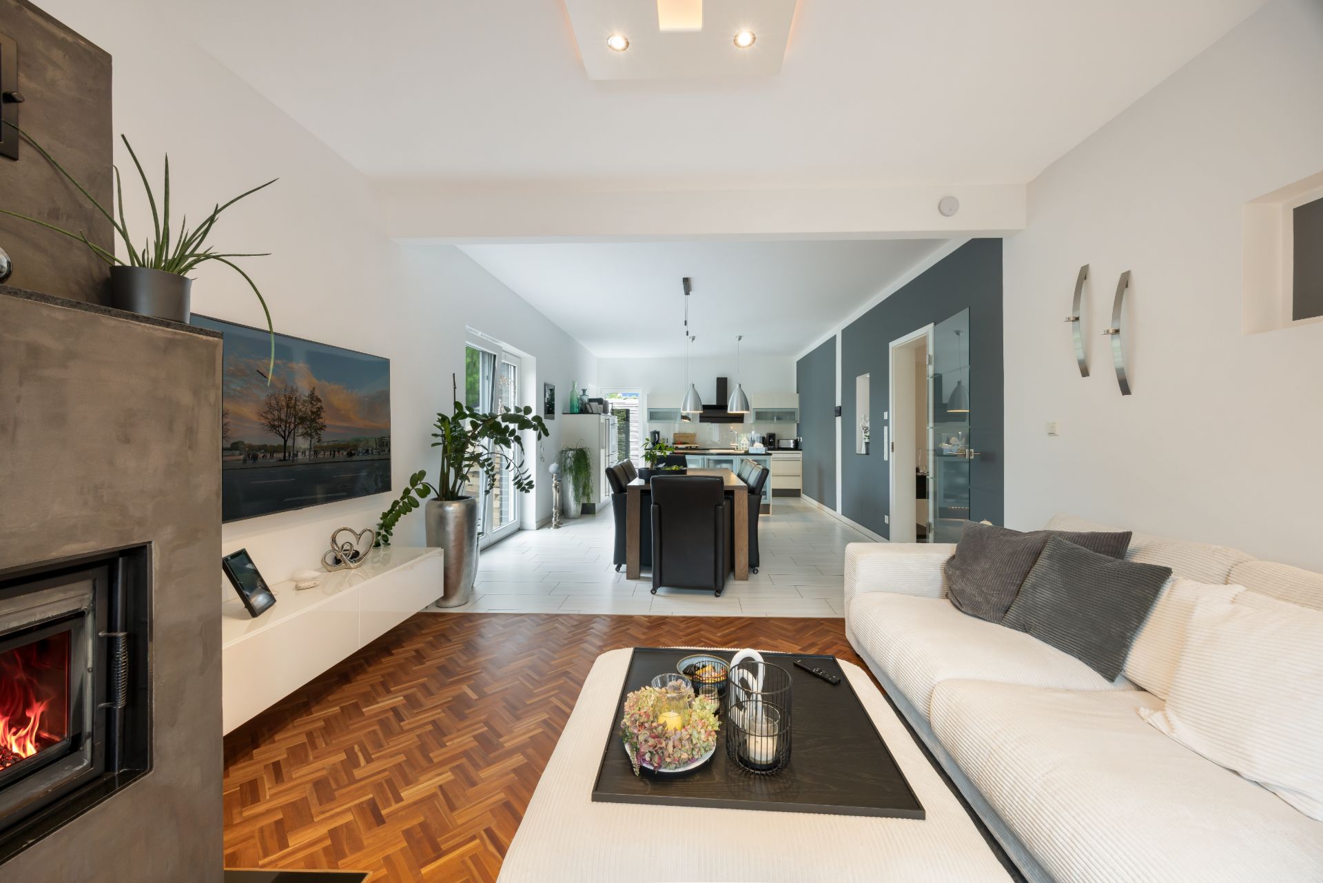Modernes Wohnzimmer mit Kamin, weißem Sofa und Blick in eine offene Küche mit Esstisch.