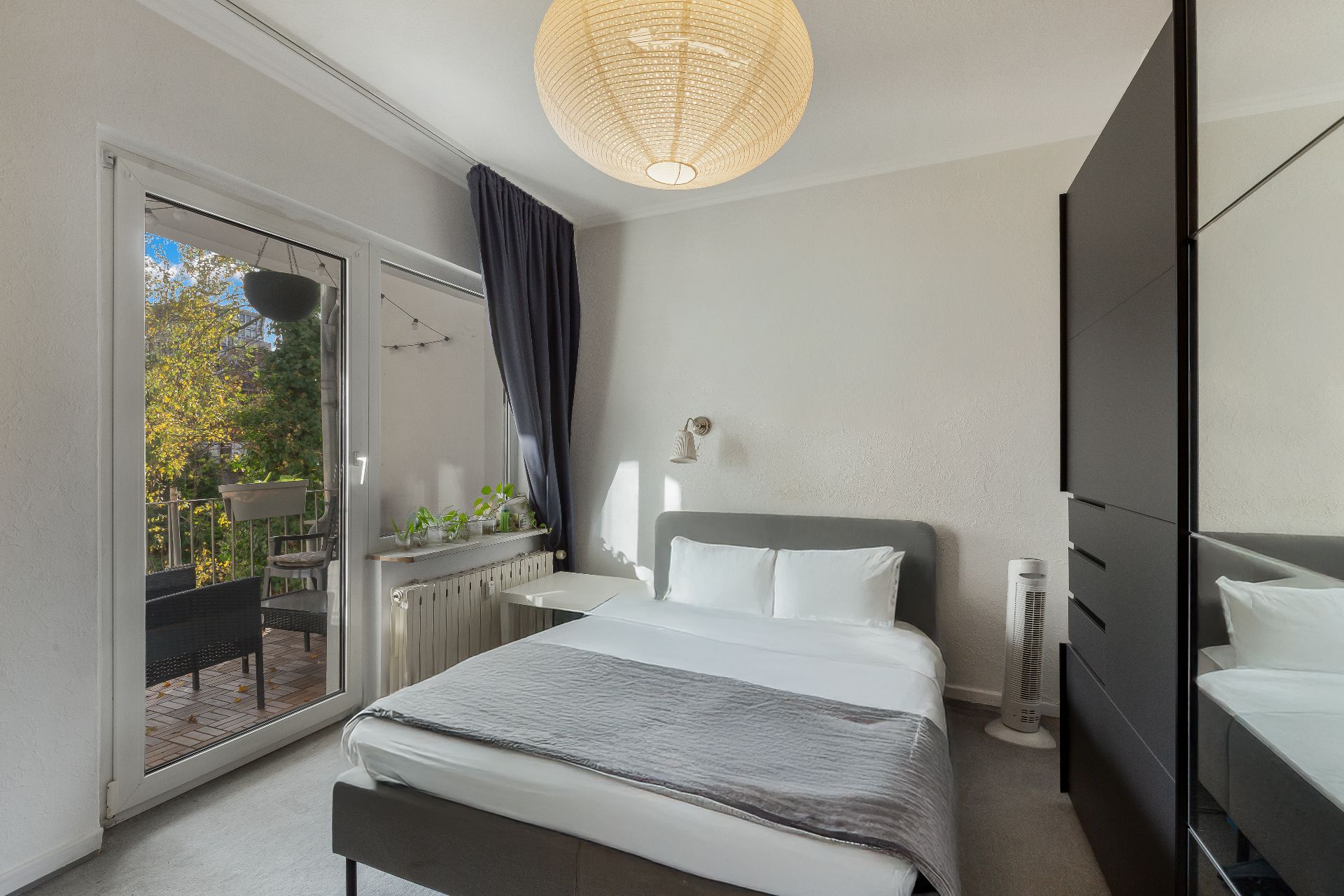 Helles Schlafzimmer mit Doppelbett, Schrank und Zugang zu einem Balkon mit Sitzmöbeln.
