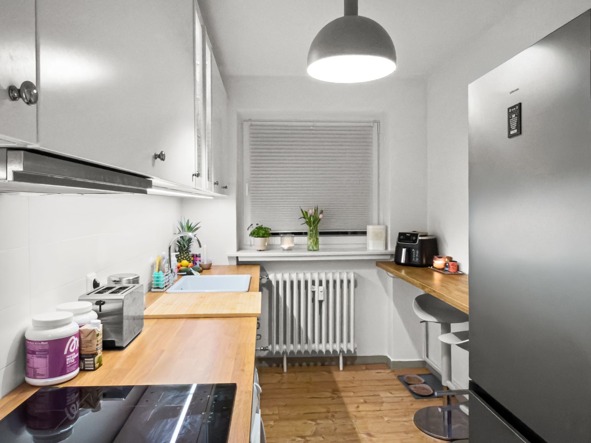 Moderne, schmale Küche mit Holzarbeitsplatten, weißen Schränken und großem Kühlschrank.