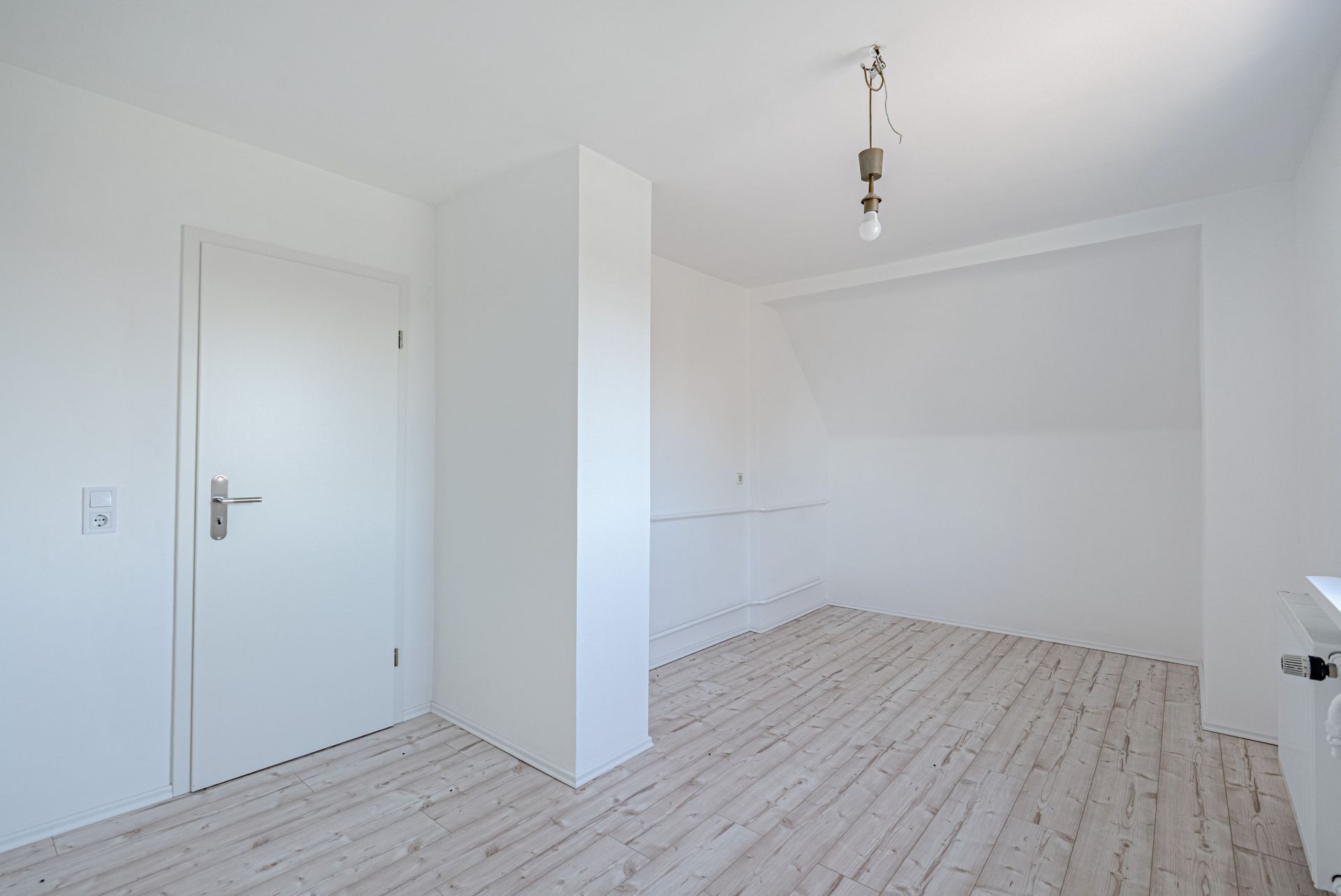 Leerer, heller Raum mit weiß gestrichenen Wänden und Holzboden.