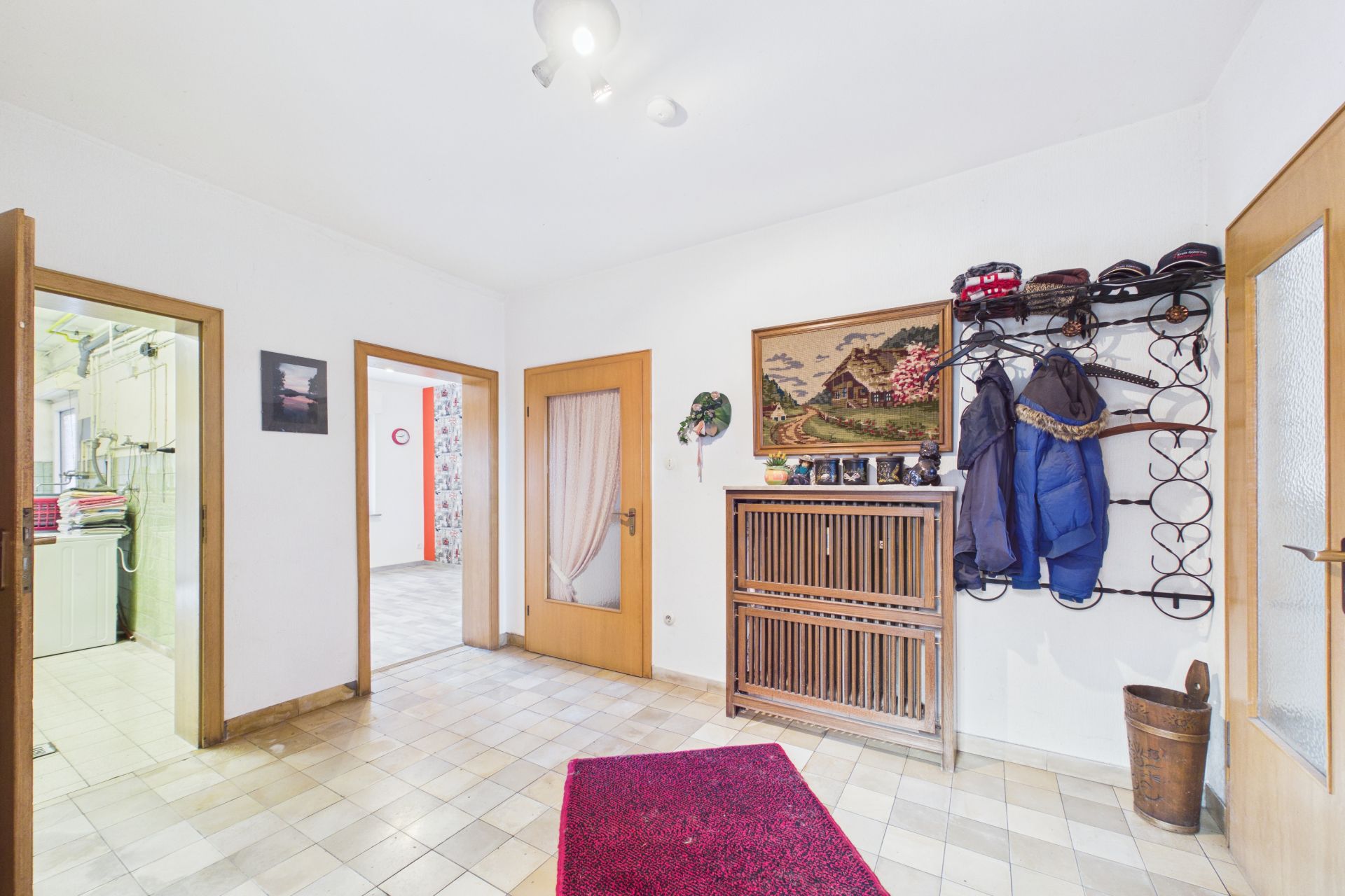 Heller Flur mit Garderobe, Holzmöbel, Wandbild und offenen Türen zu angrenzenden Räumen.