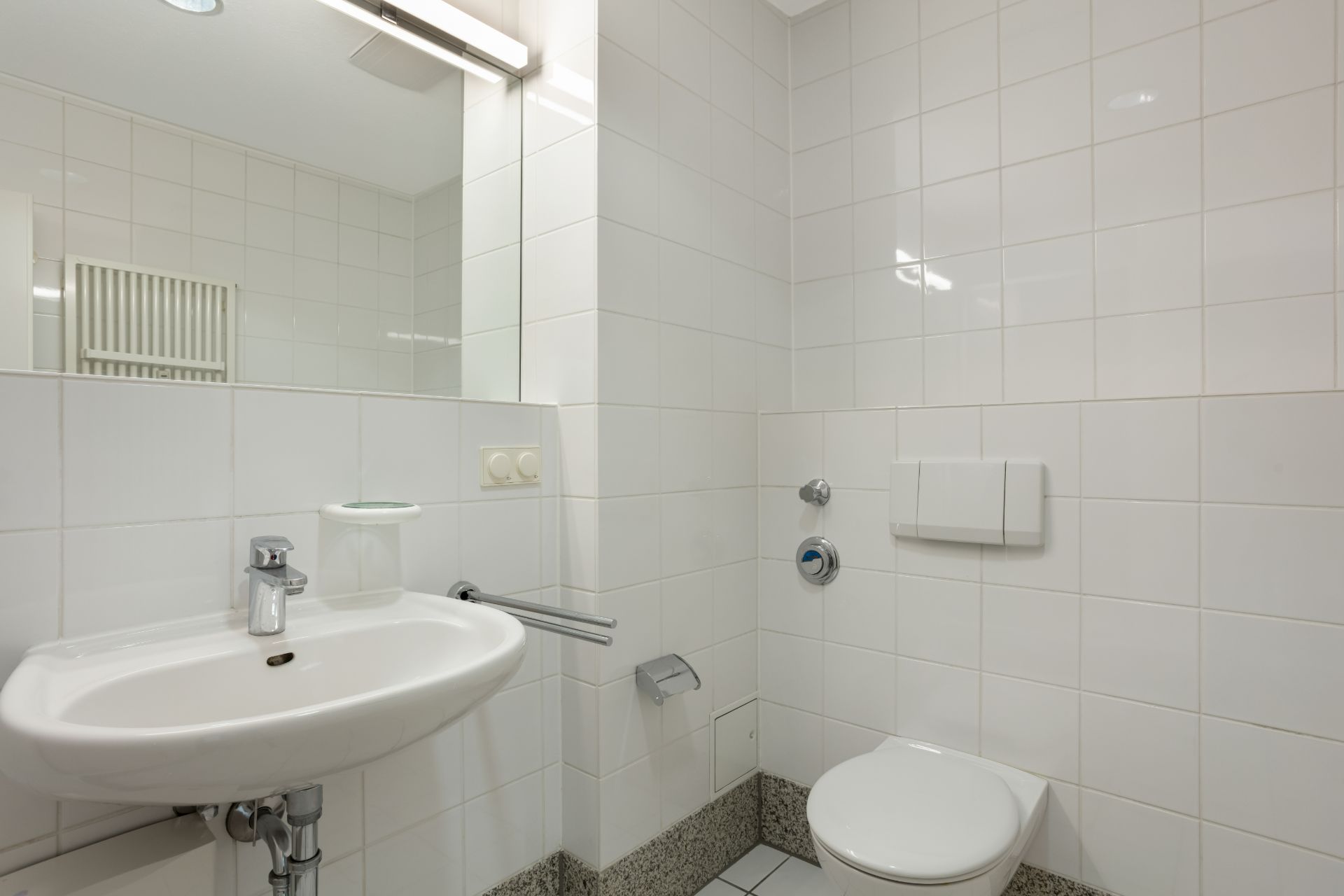 Modernes Badezimmer mit weiß gefliesten Wänden, Waschbecken, Spiegel und WC.