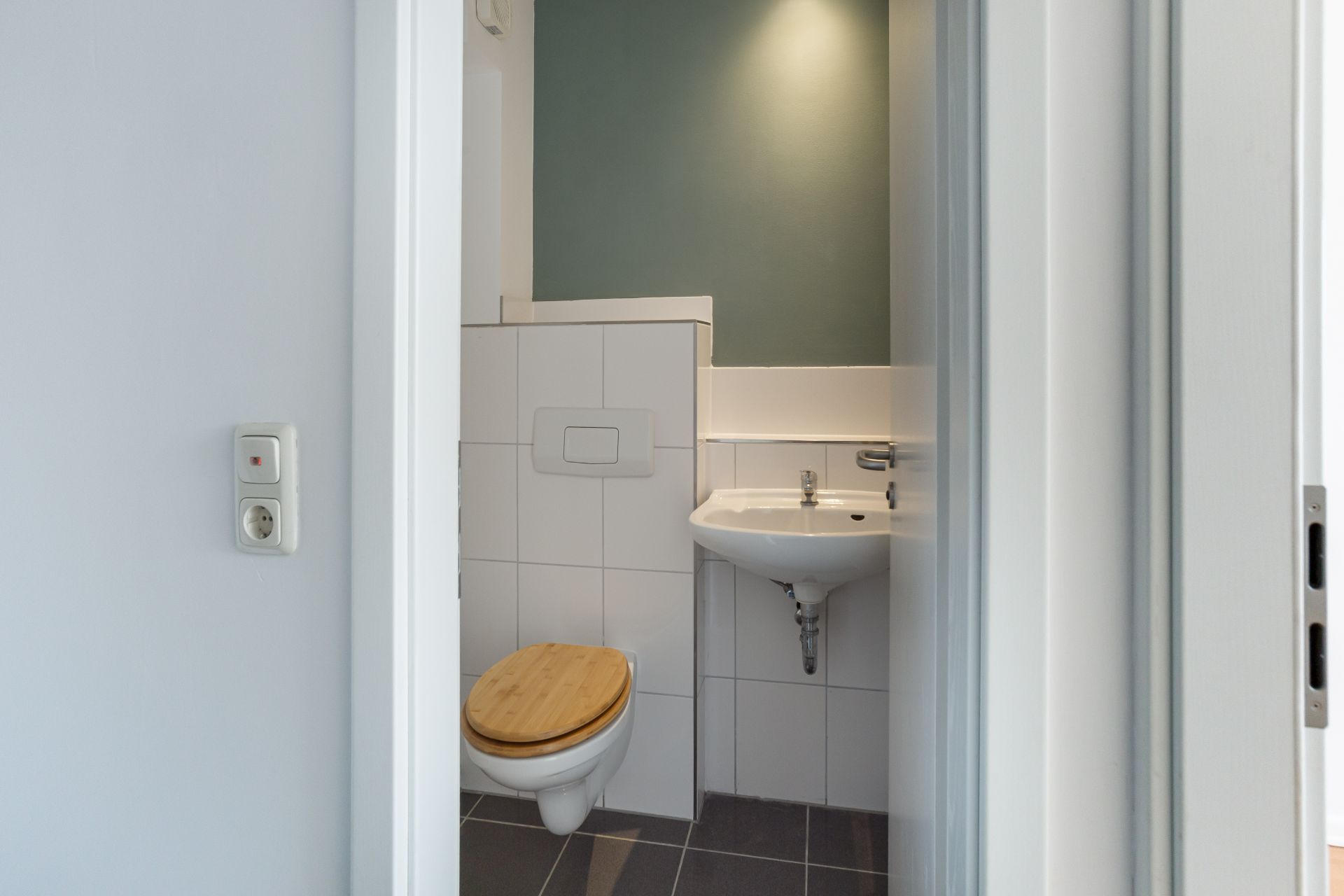 Kleines Badezimmer mit WC und Waschbecken, weißen Fliesen und Holz-Toilettensitz.