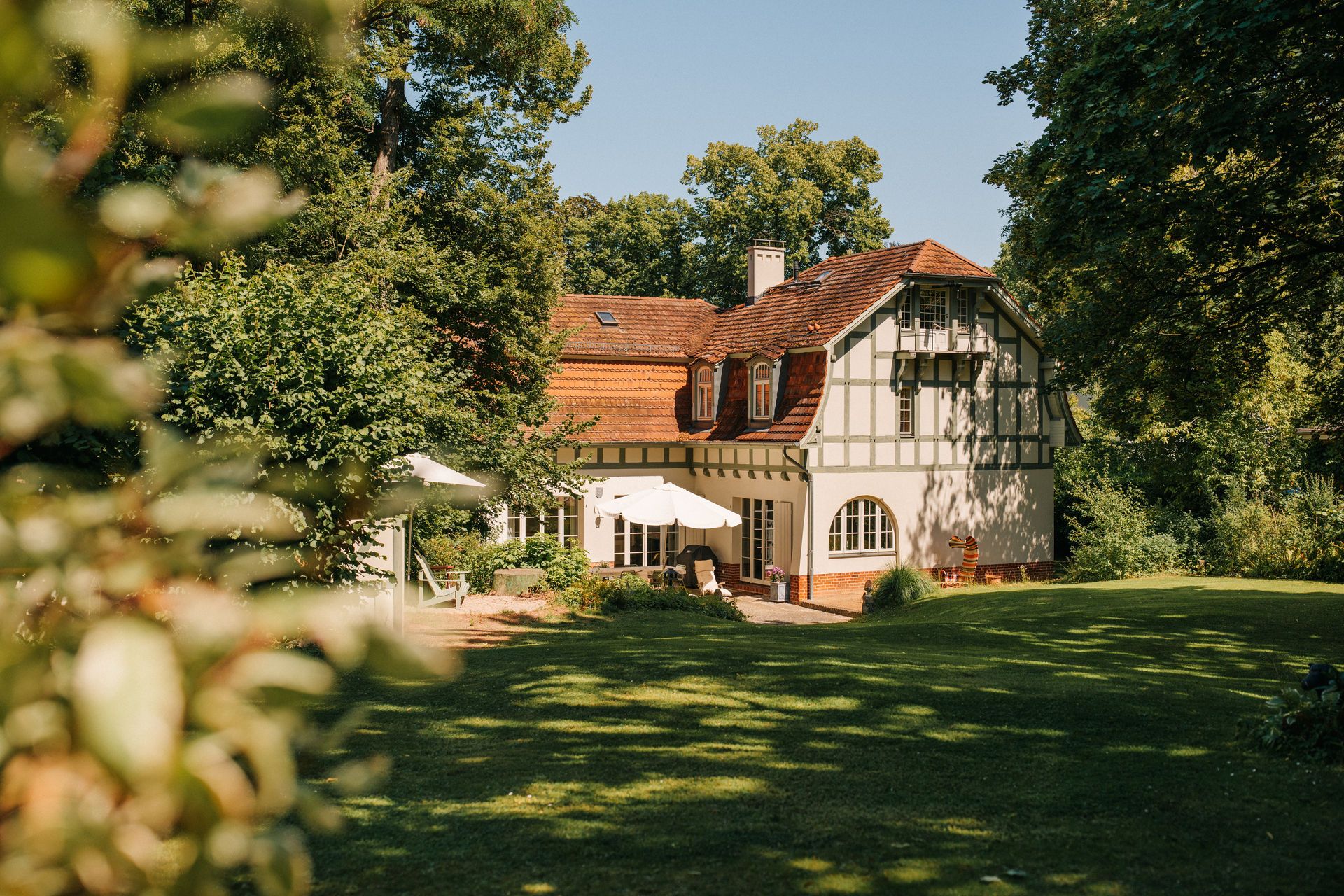 Zweistöckiges Haus mit rotem Dach und Garten, umgeben von Bäumen bei sonnigem Wetter.