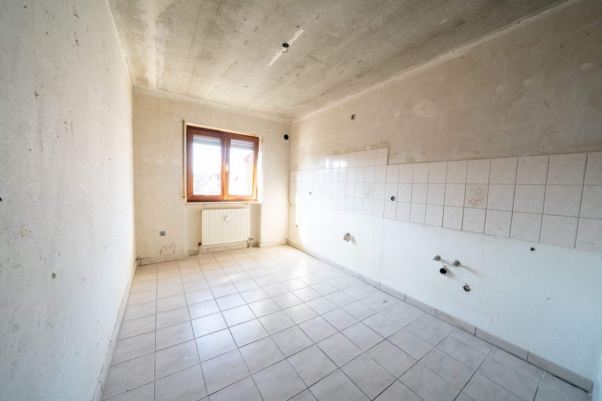 Leerer, gefliester Raum mit Fenster und Heizung, Wandfliesen auf einer Seite.