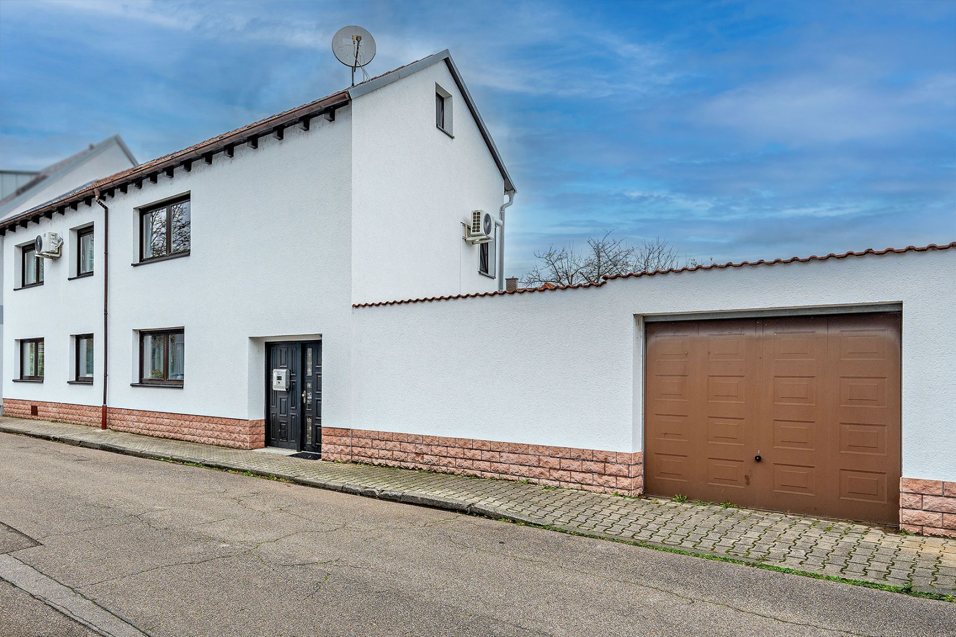 Weißes Wohnhaus mit braunem Garagentor und mehreren Fenstern an einer ruhigen Straße.