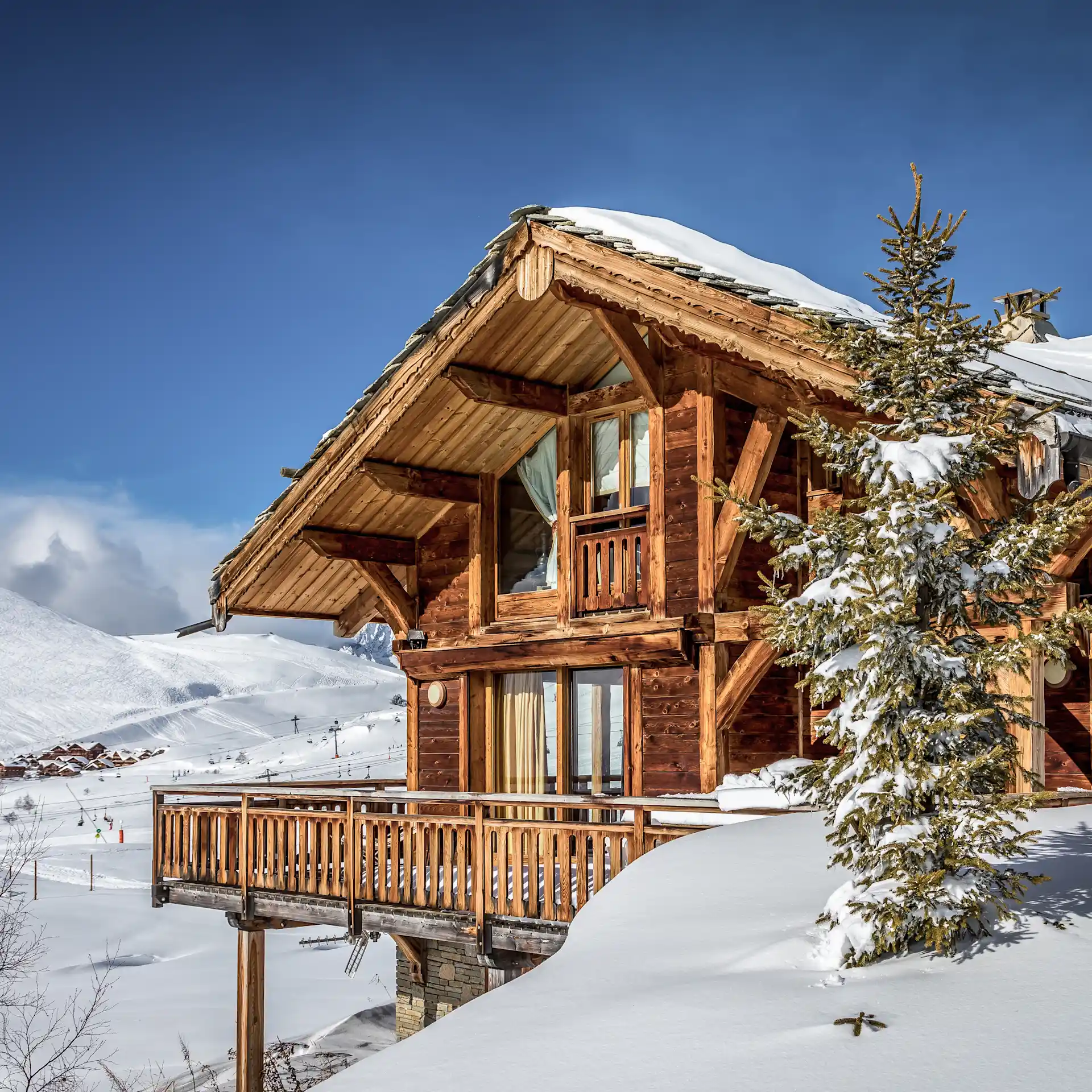 Holzchalet im Schnee mit Balkon und großen Fenstern, Berge im Hintergrund.