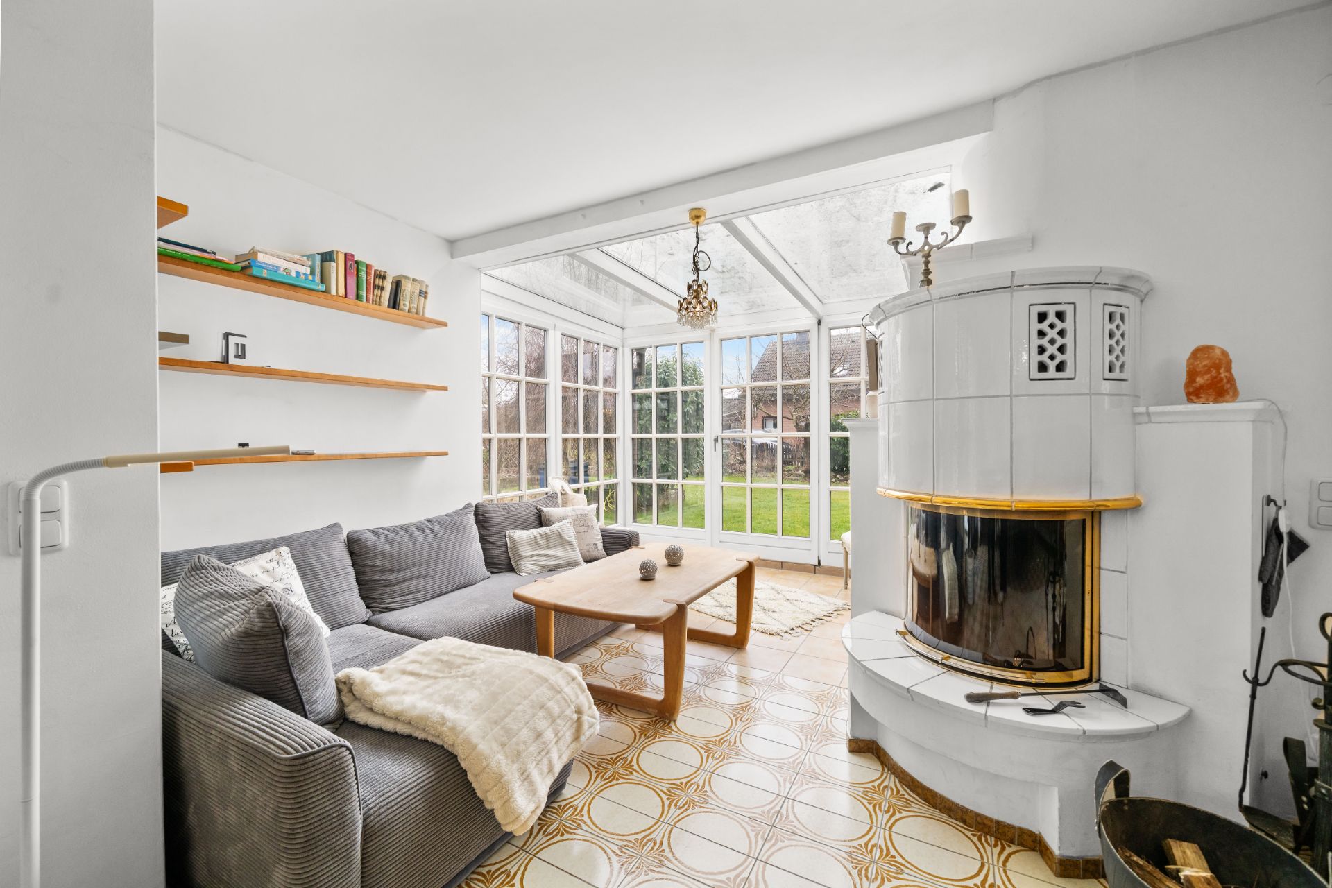Helles Wohnzimmer mit Ecksofa, Kamin, Couchtisch und großen Fenstern zum Garten.