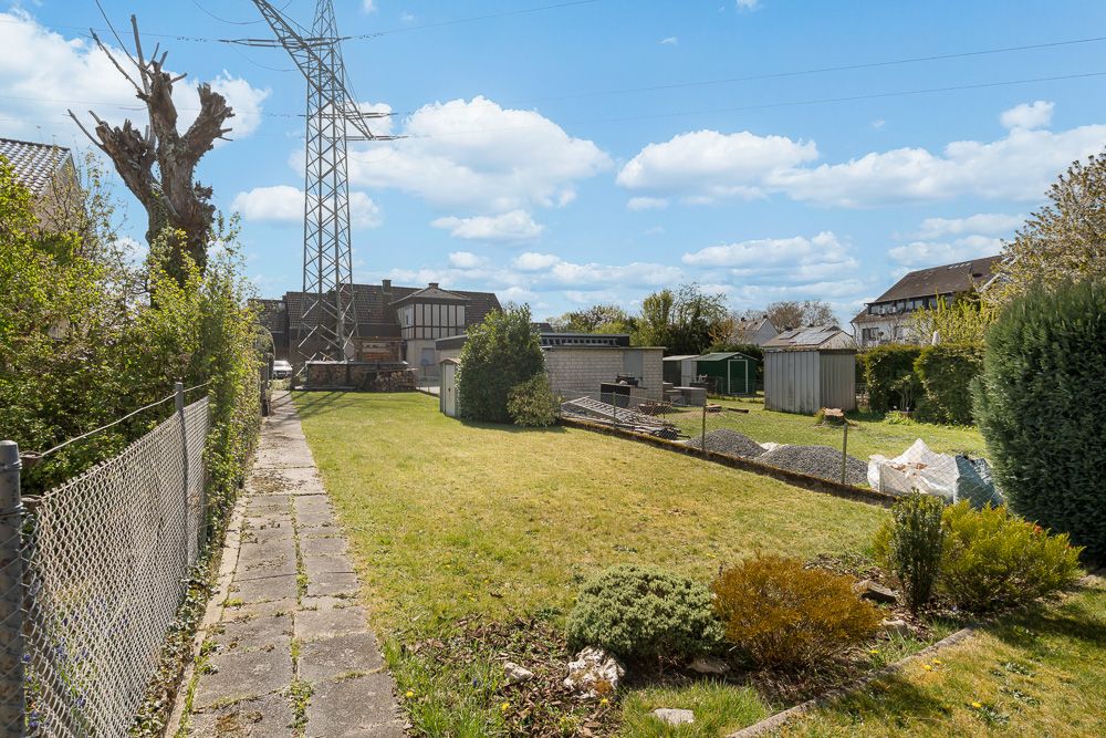 Garten mit Rasenfläche, Gehweg, Sträuchern, Schuppen und Strommast im Hintergrund.