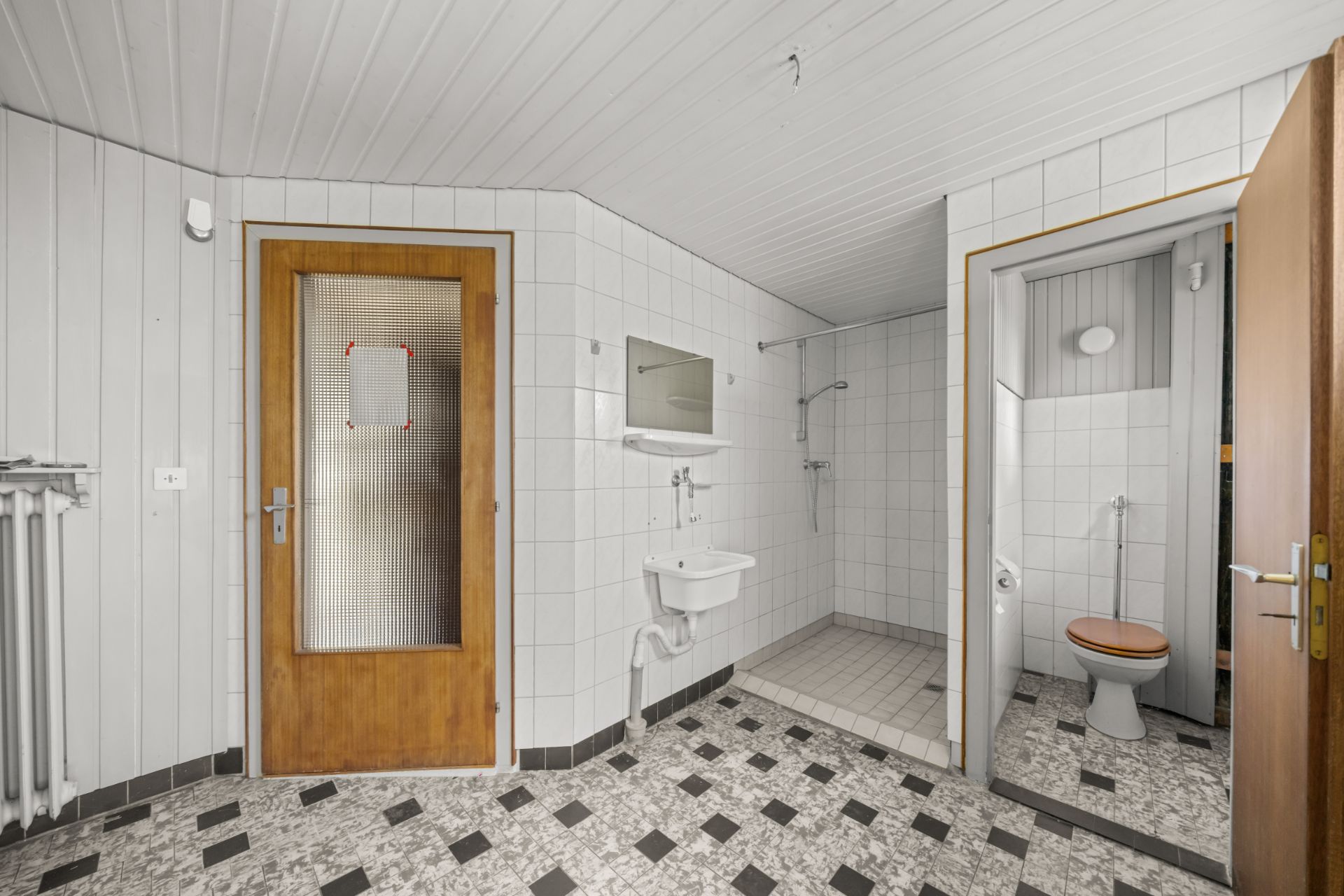 Badezimmer mit Waschbecken, Spiegel, Dusche und separatem WC mit Holztür.