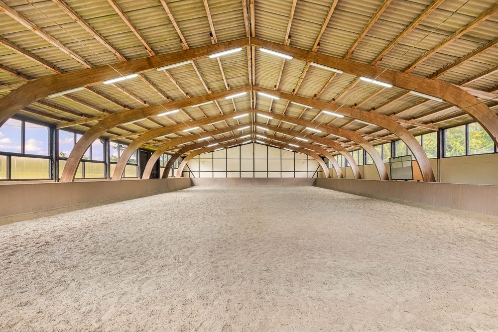 Große, helle Reithalle mit Sandboden und Holzbalken unter dem Dach.