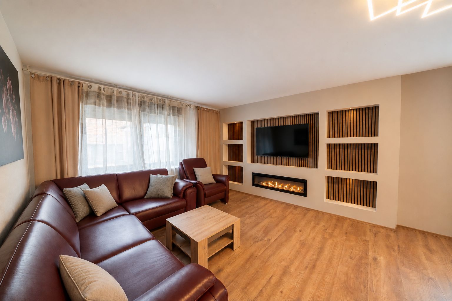 Wohnzimmer mit Ecksofa, Couchtisch, Fernseher und elektrischem Kamin auf Holzboden.