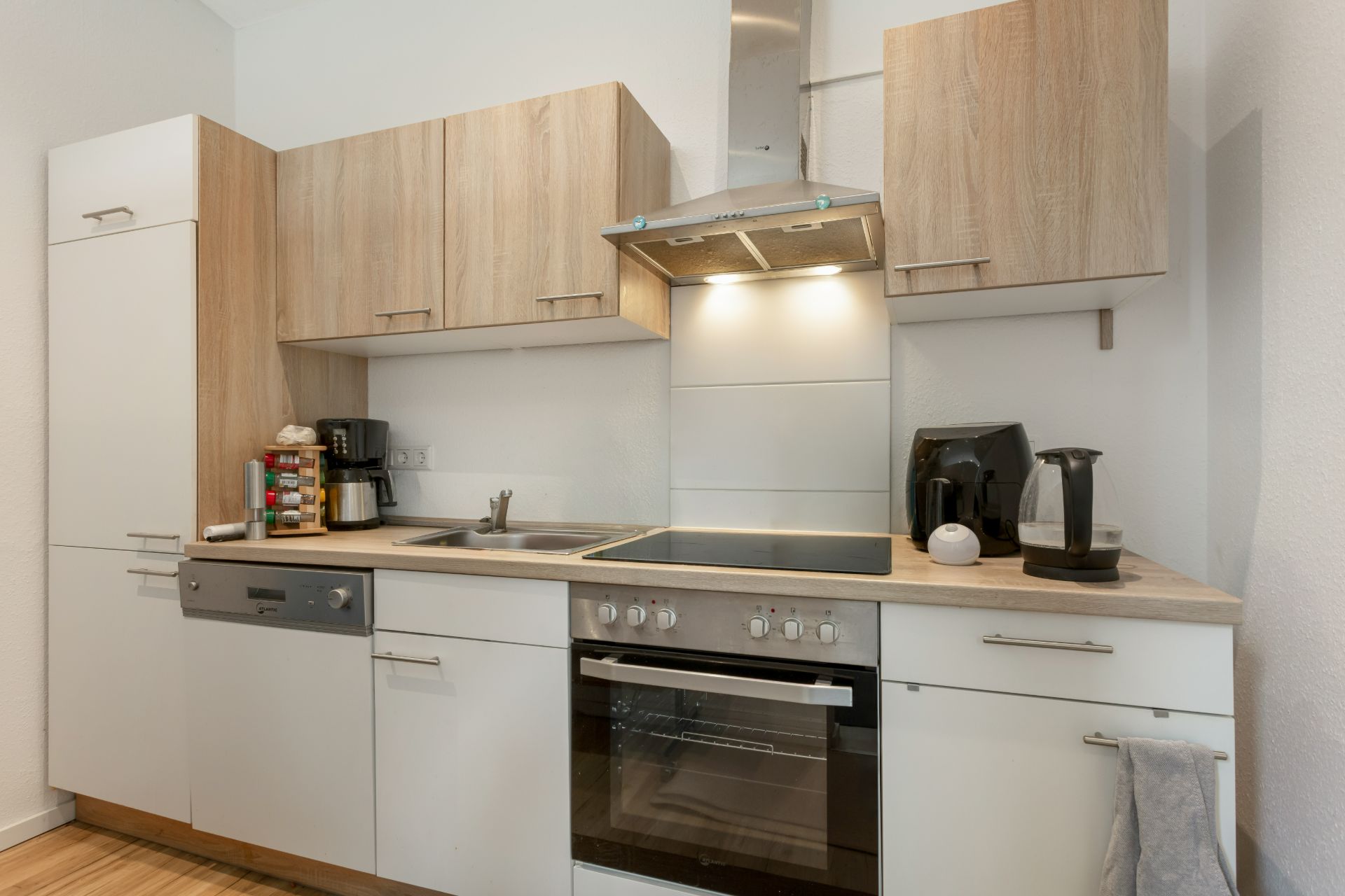 Moderne Einbauküche mit Herd, Backofen, Spüle, Kaffeemaschine und Wasserkocher.