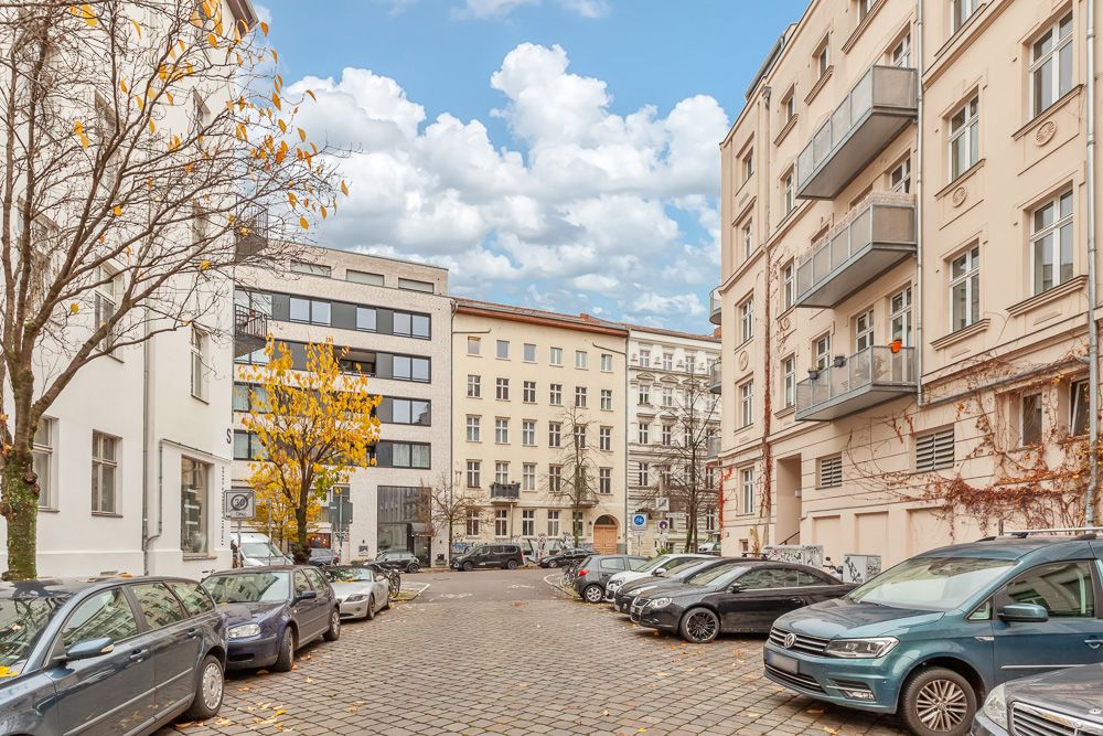 Mehrstöckige Wohnhäuser mit Balkonen und parkenden Autos auf einer Kopfsteinpflasterstraße.