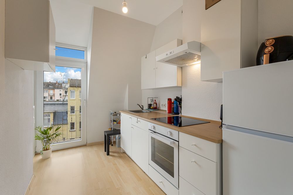 Helle, schmale Küche mit Herd, Ofen, Kühlschrank und großem Fenster mit Blick nach draußen.