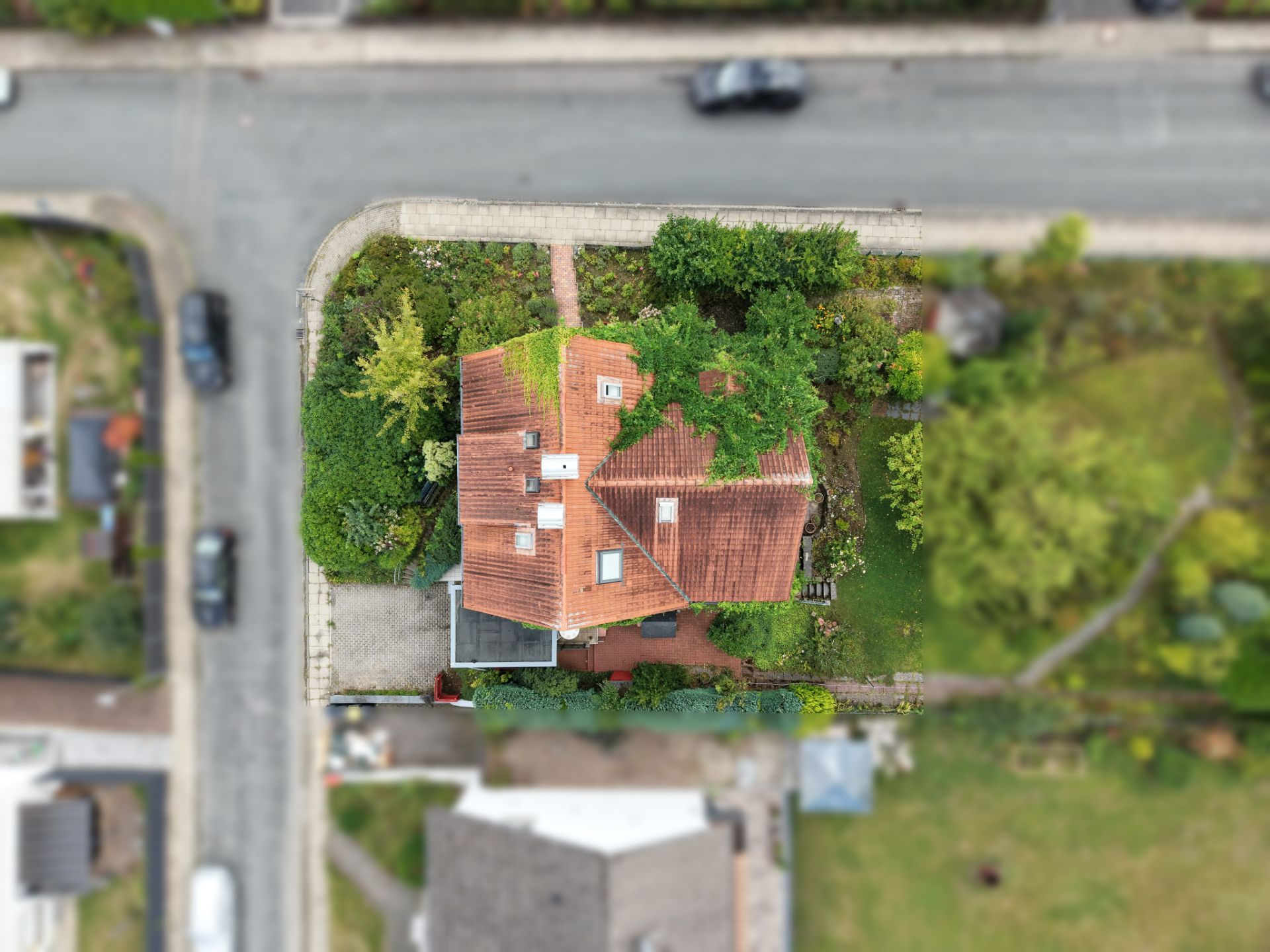 Luftaufnahme eines Hauses mit rotem Dach, umgeben von Garten und Straße.