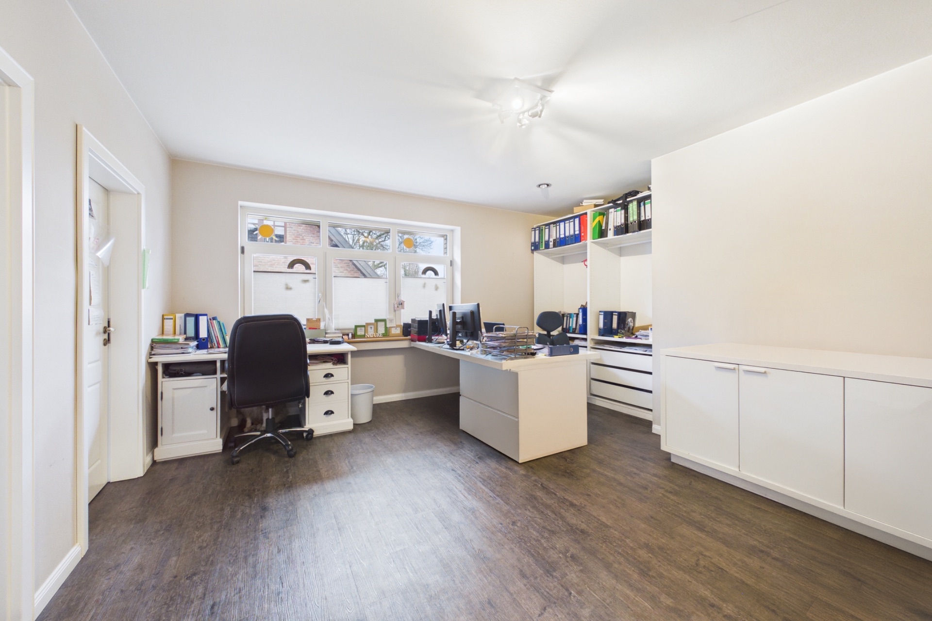 Helles Arbeitszimmer mit zwei Schreibtischen, Regalen und Fenster mit Blick nach draußen.