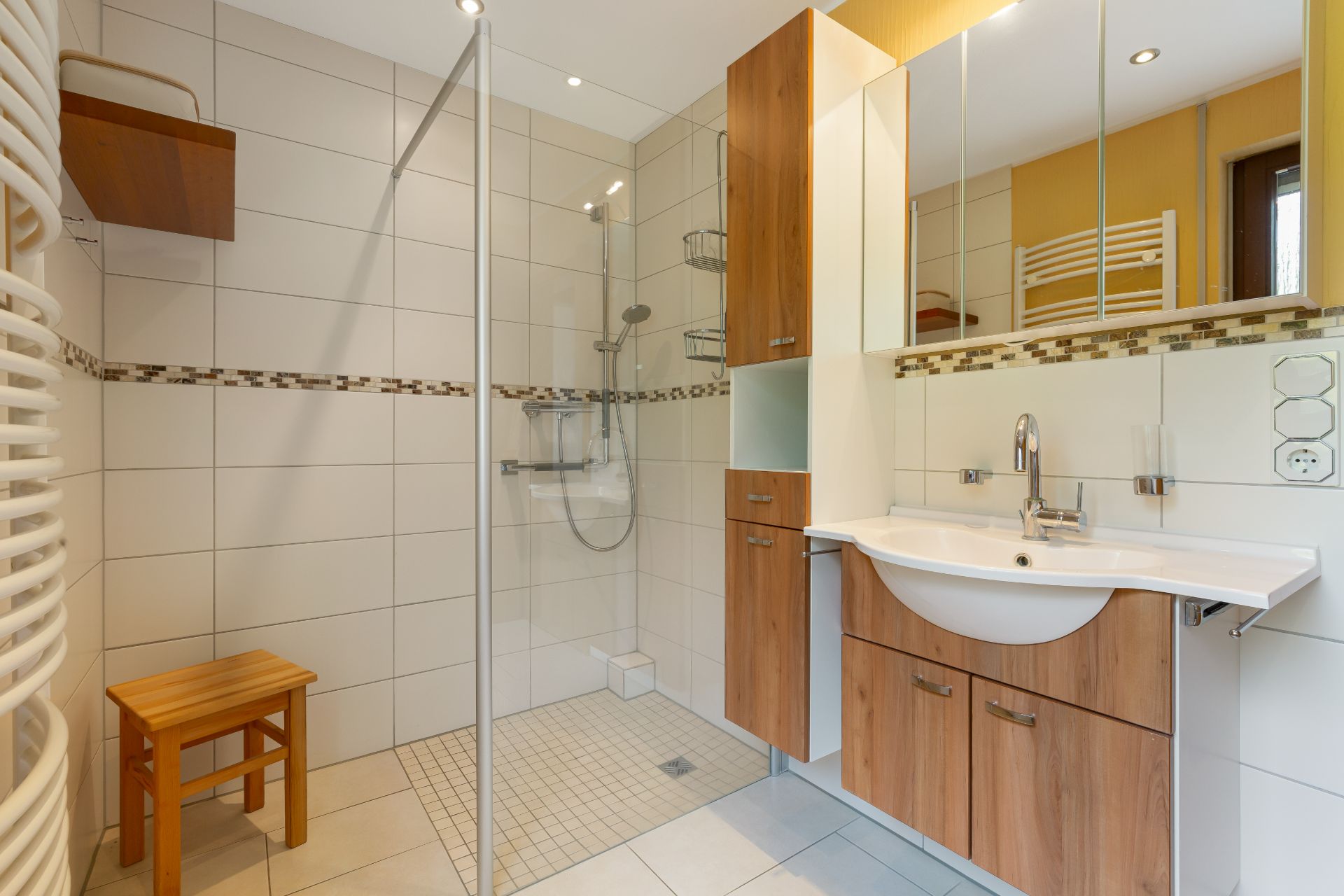 Modernes Badezimmer mit bodengleicher Dusche, Holzschrank, Waschbecken und Wandspiegel.