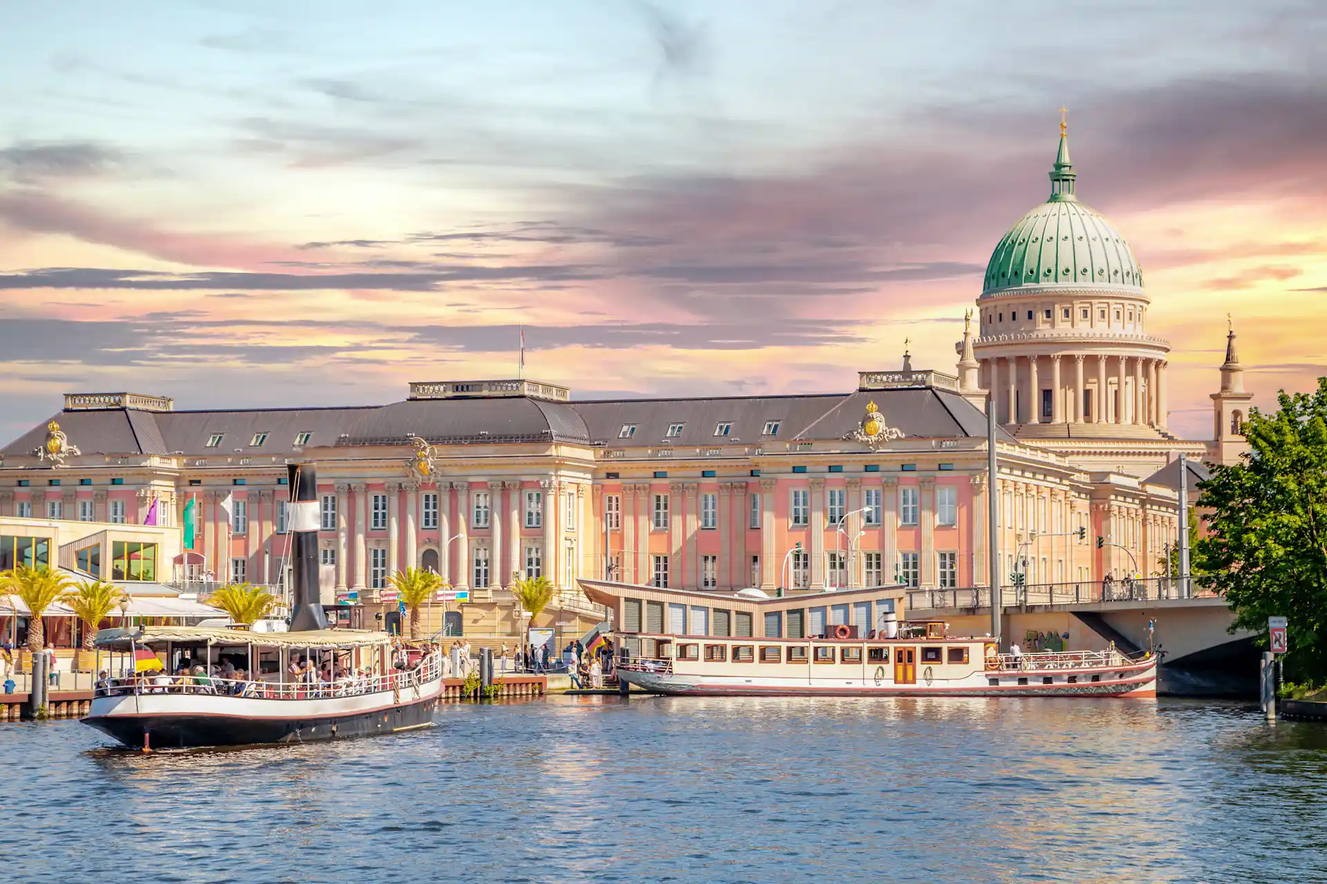 Großes historisches Gebäude mit Kuppel und Booten auf einem Fluss bei Sonnenuntergang.