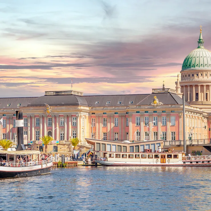 Großes historisches Gebäude mit Kuppel und Booten auf einem Fluss bei Sonnenuntergang.