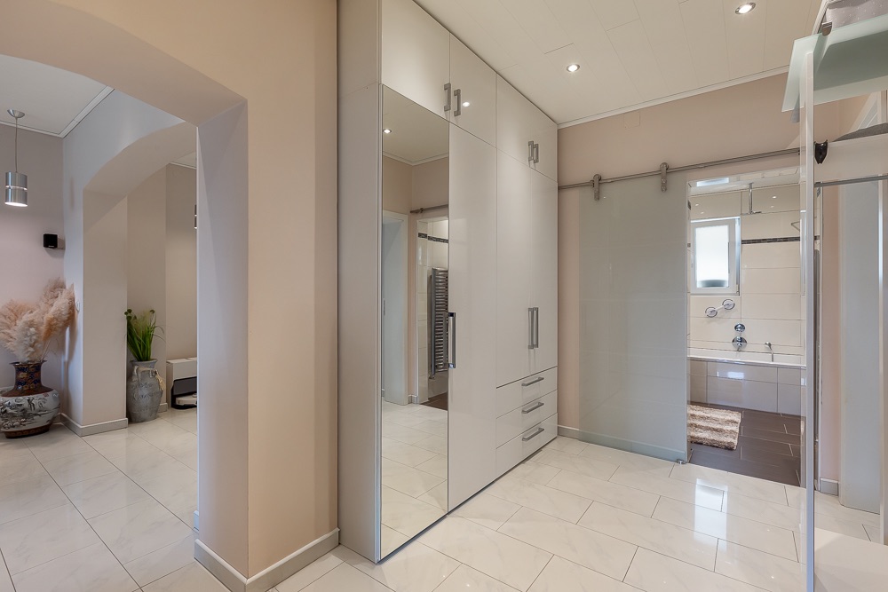 Heller Flur mit Einbauschrank, Spiegel und Zugang zum Badezimmer mit Badewanne.