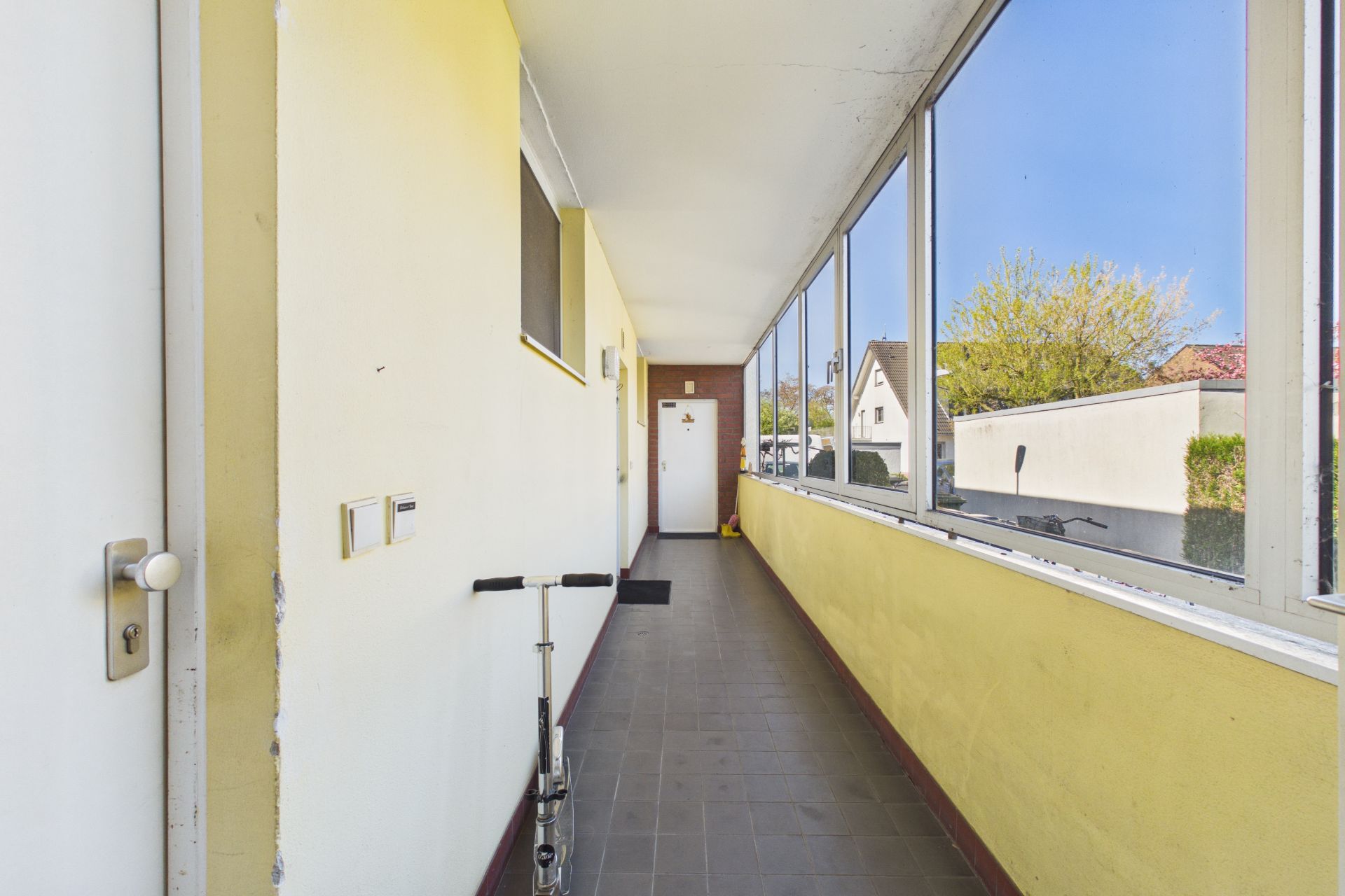 Langer, verglaster Flur mit gelben Wänden und einem Roller an der Wand.