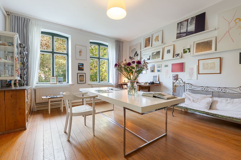 Helles Wohnzimmer mit Holzboden, großem Tisch, Stuhl, Sofa und vielen Bildern an der Wand.