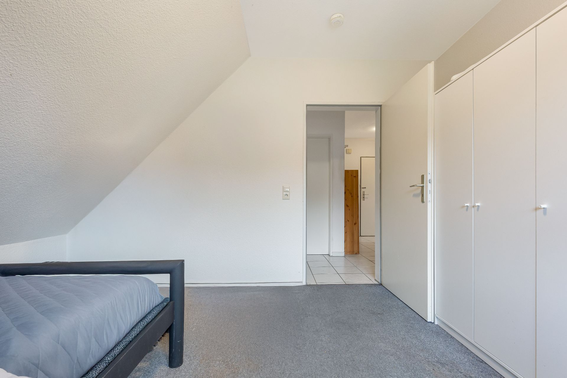 Helles Schlafzimmer mit Bett, Teppichboden und weißem Kleiderschrank.