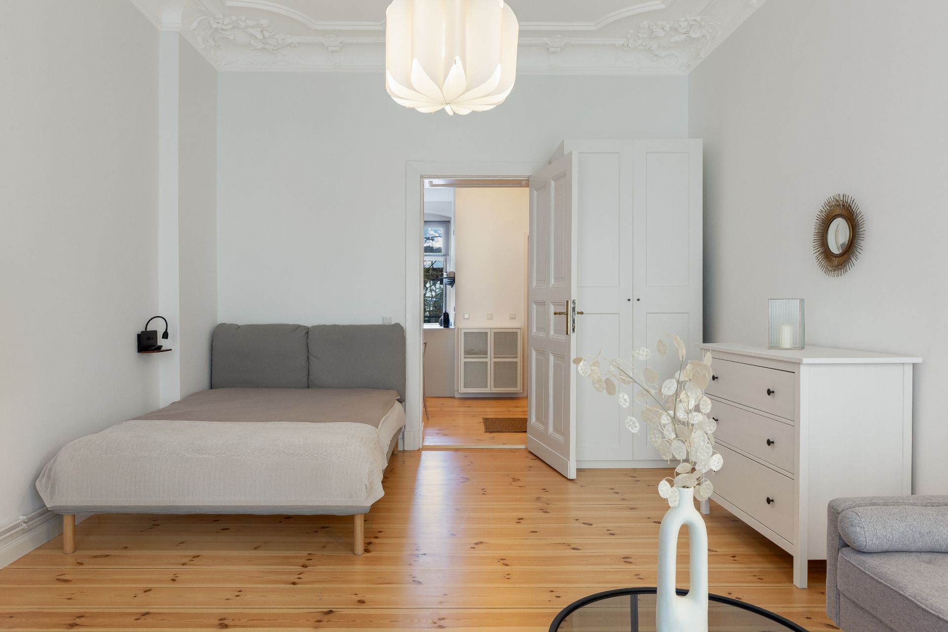 Helles Schlafzimmer mit Bett, weißem Schrank, Kommode und Holzboden.
