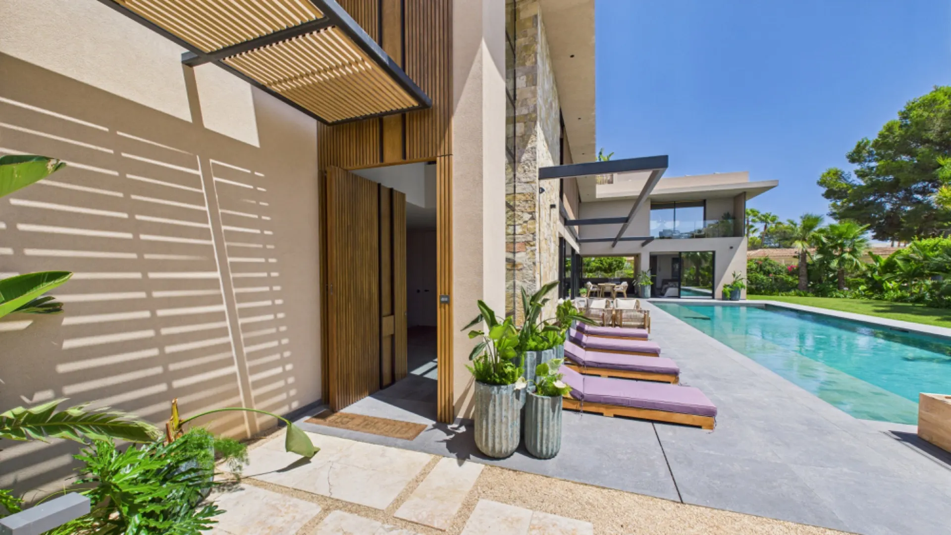 Moderner Garten mit Pool, Liegen und Pflanzen neben einem Wohnhaus bei sonnigem Wetter.
