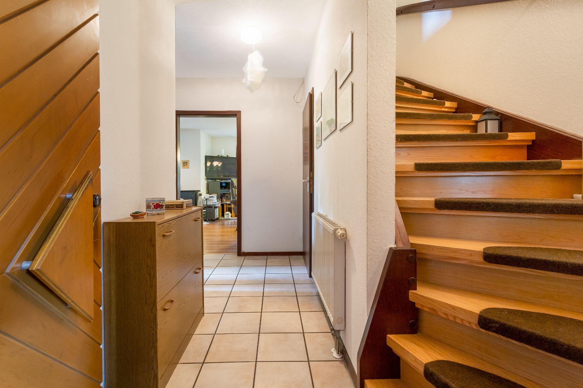 Heller Flur mit gefliester Boden, Holztreppe rechts und Kommode links.