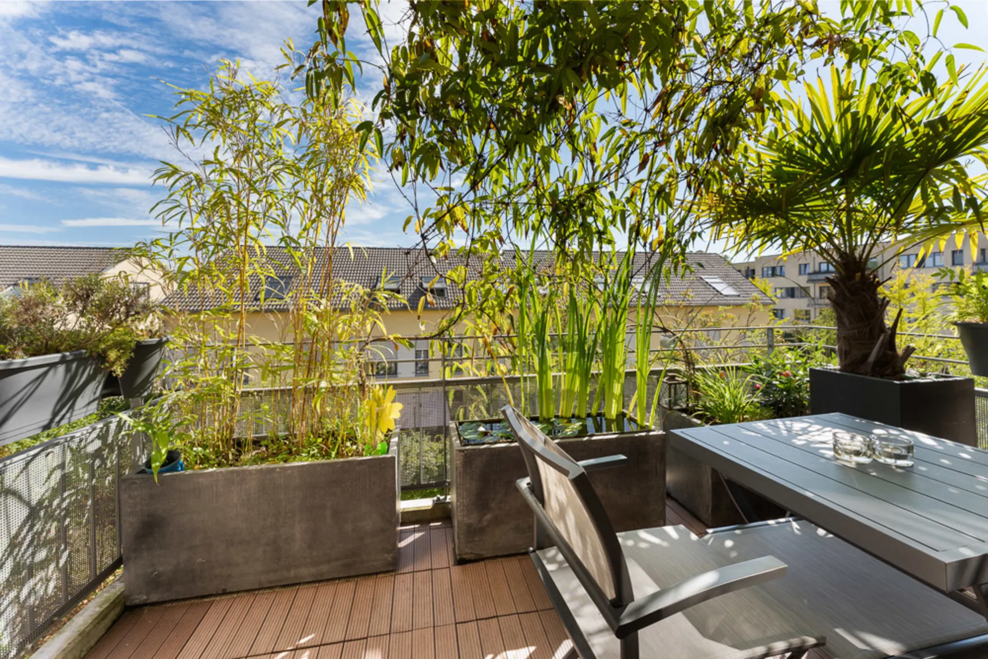 Moderne Terrasse mit Holzboden, Esstisch, Stühlen und vielen Pflanzen in großen Kübeln.