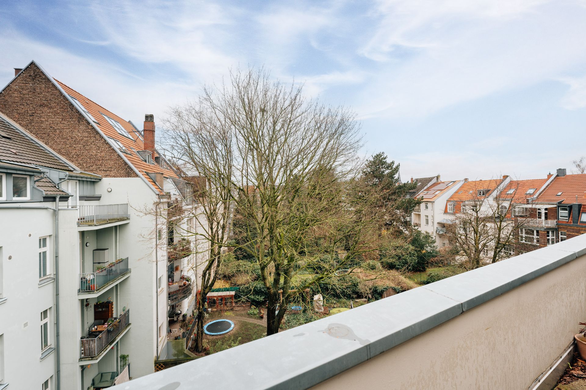 Blick von einem Balkon auf einen grünen Innenhof mit Bäumen und umliegenden Wohnhäusern.
