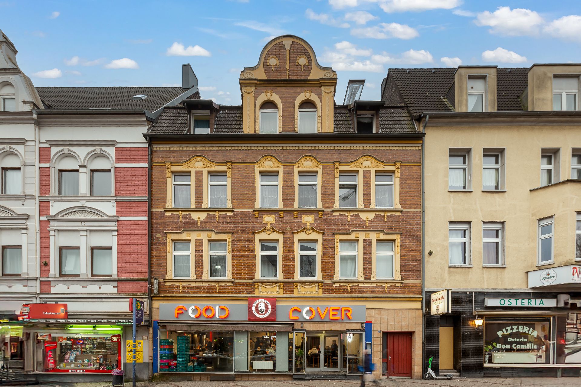 Dreistöckiges Wohnhaus mit roter Fassade und Ladengeschäften im Erdgeschoss.