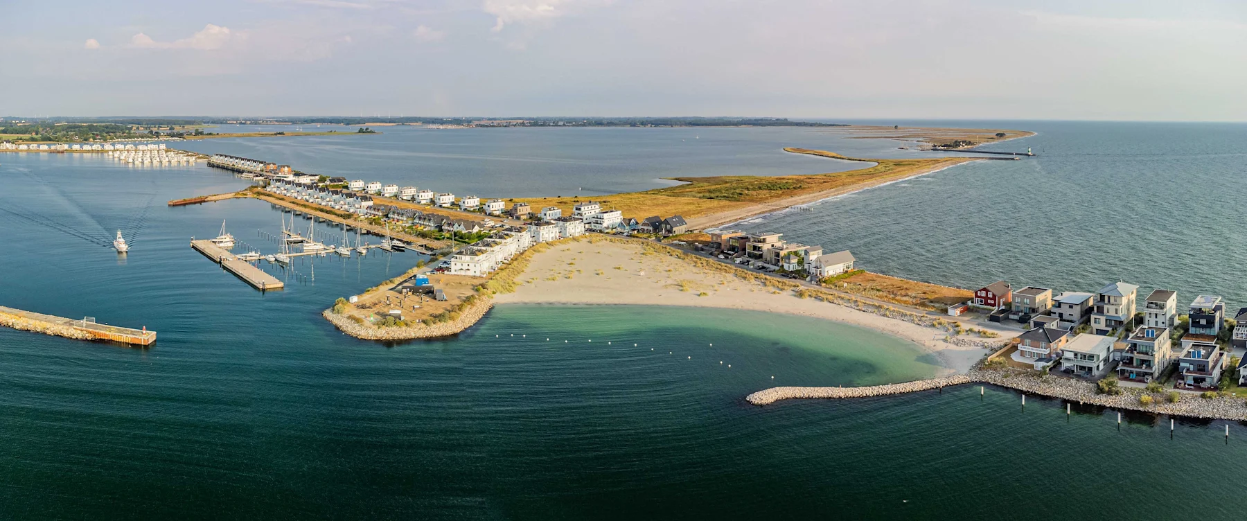 Luftaufnahme von modernen Häusern an einer Küste mit Sandstrand und Yachthafen.