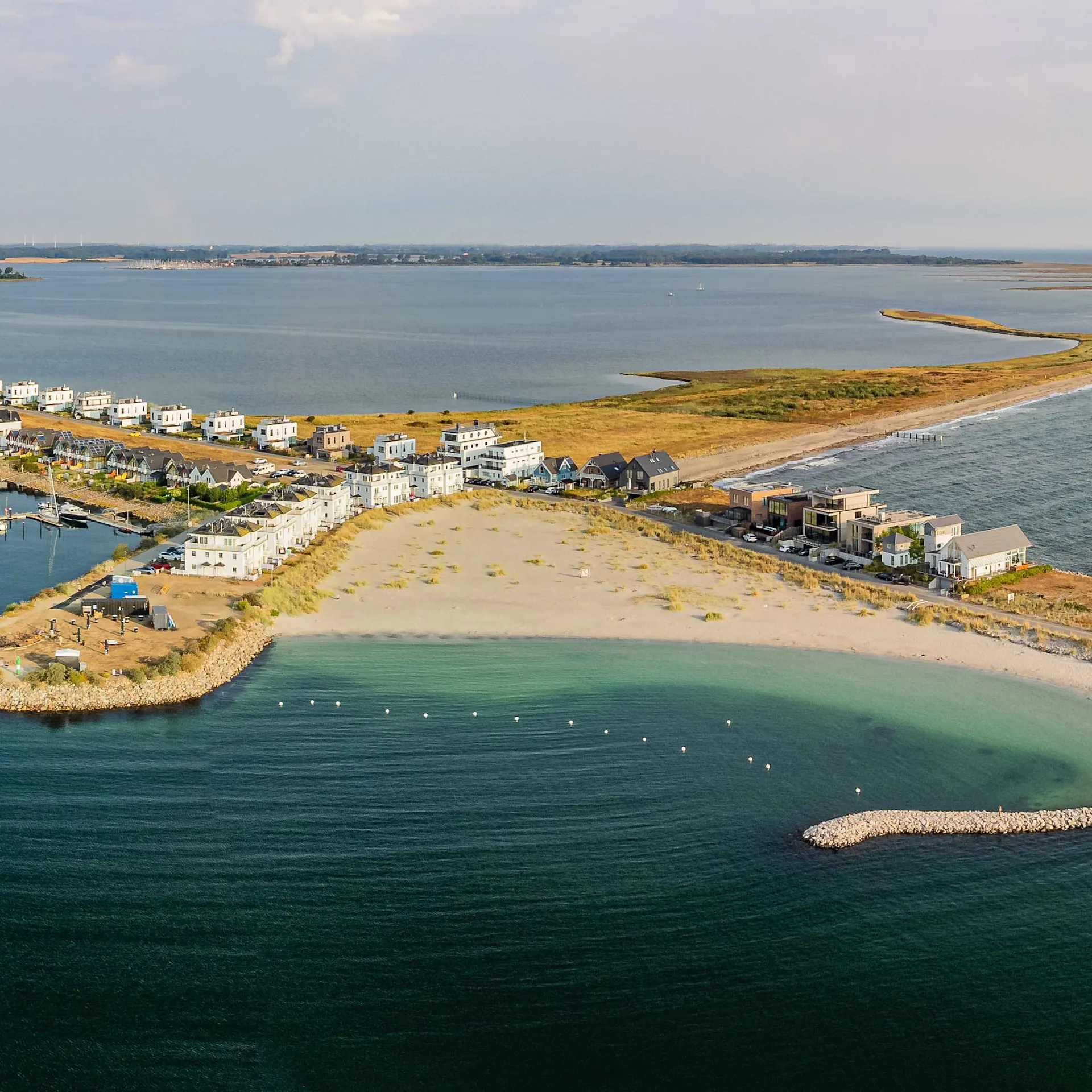 Luftaufnahme von modernen Häusern an einer Küste mit Sandstrand und Yachthafen.