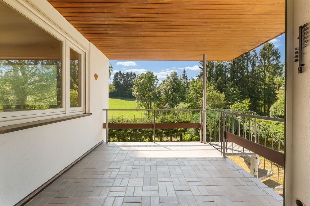 Überdachte Terrasse mit Fliesenboden und Ausblick auf einen grünen Garten und Bäume.