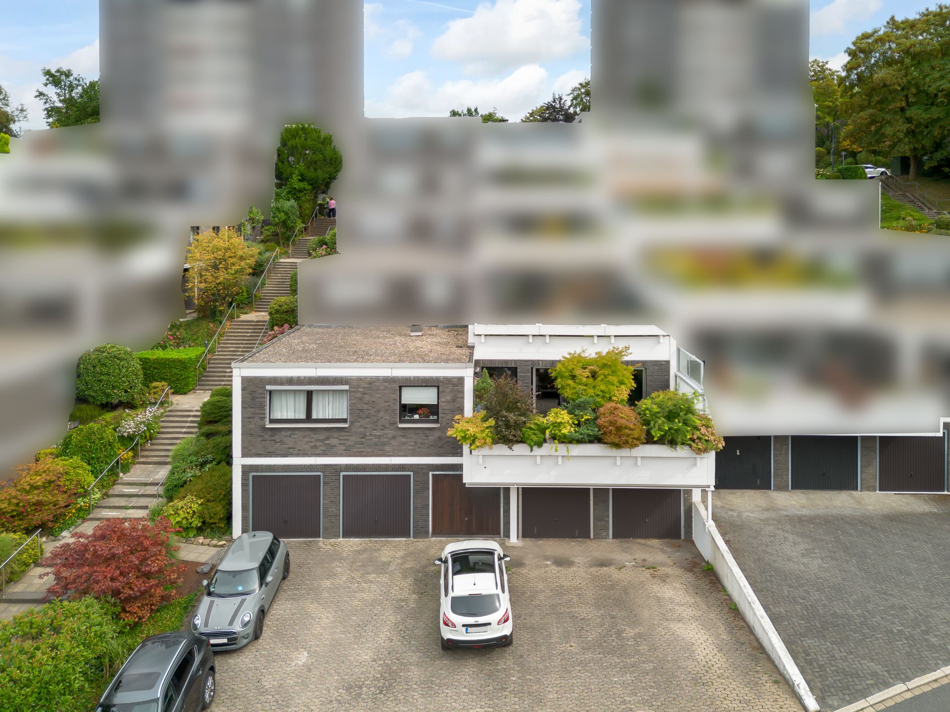 Zweistöckiges Wohnhaus mit drei Garagen, bepflanztem Balkon und drei geparkten Autos davor.