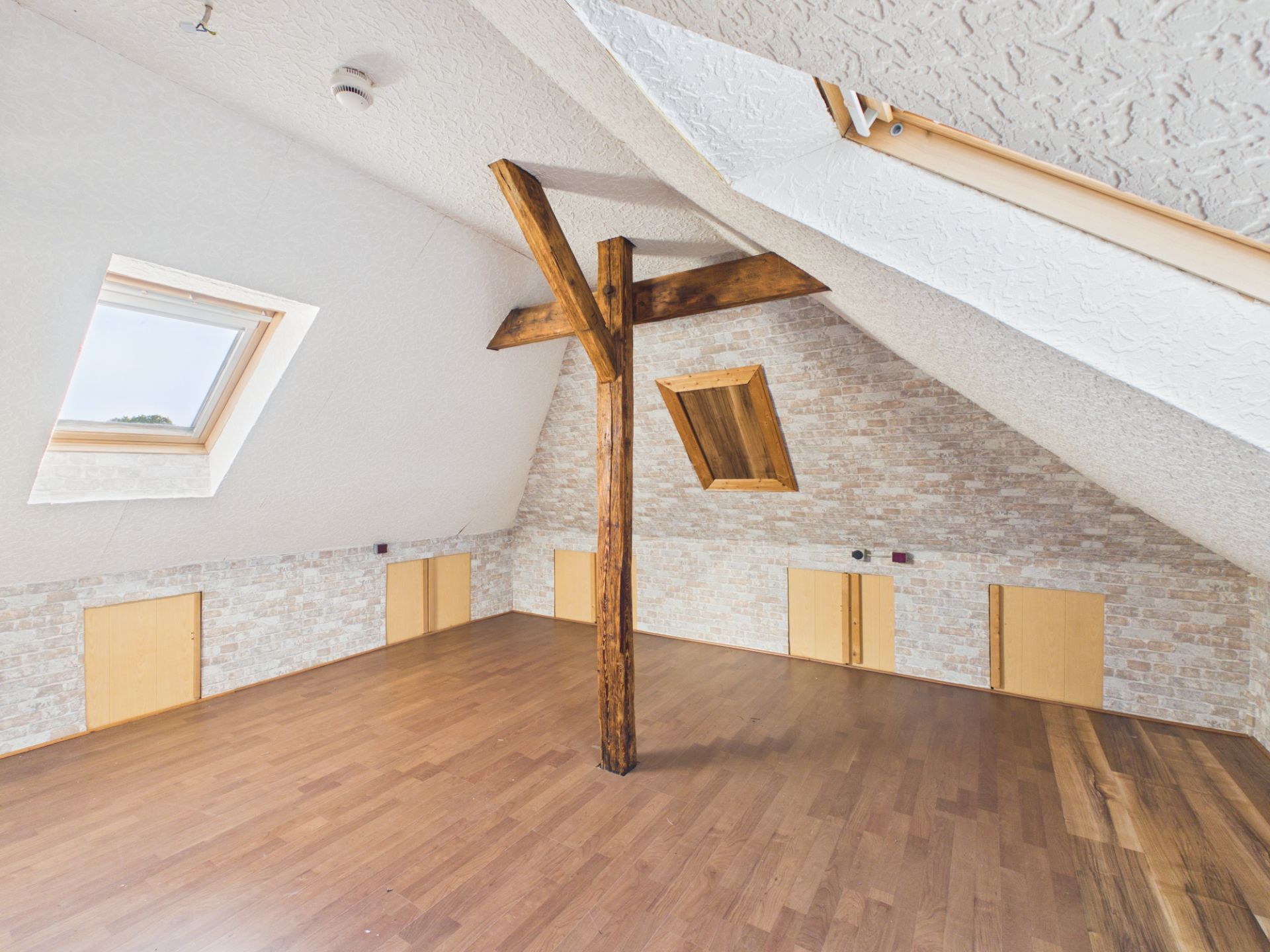 Dachzimmer mit Holzboden, sichtbarem Balken und mehreren Dachfenstern.
