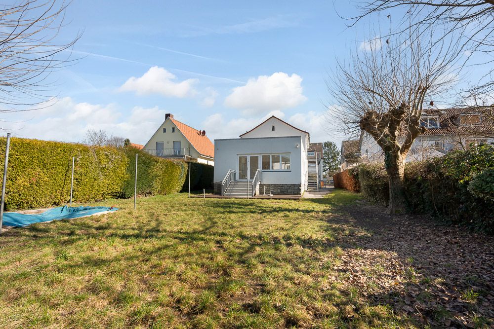 Rückansicht eines Hauses mit großem Garten, Rasenfläche und Bäumen, daneben Hecke und Nachbarhäuser.