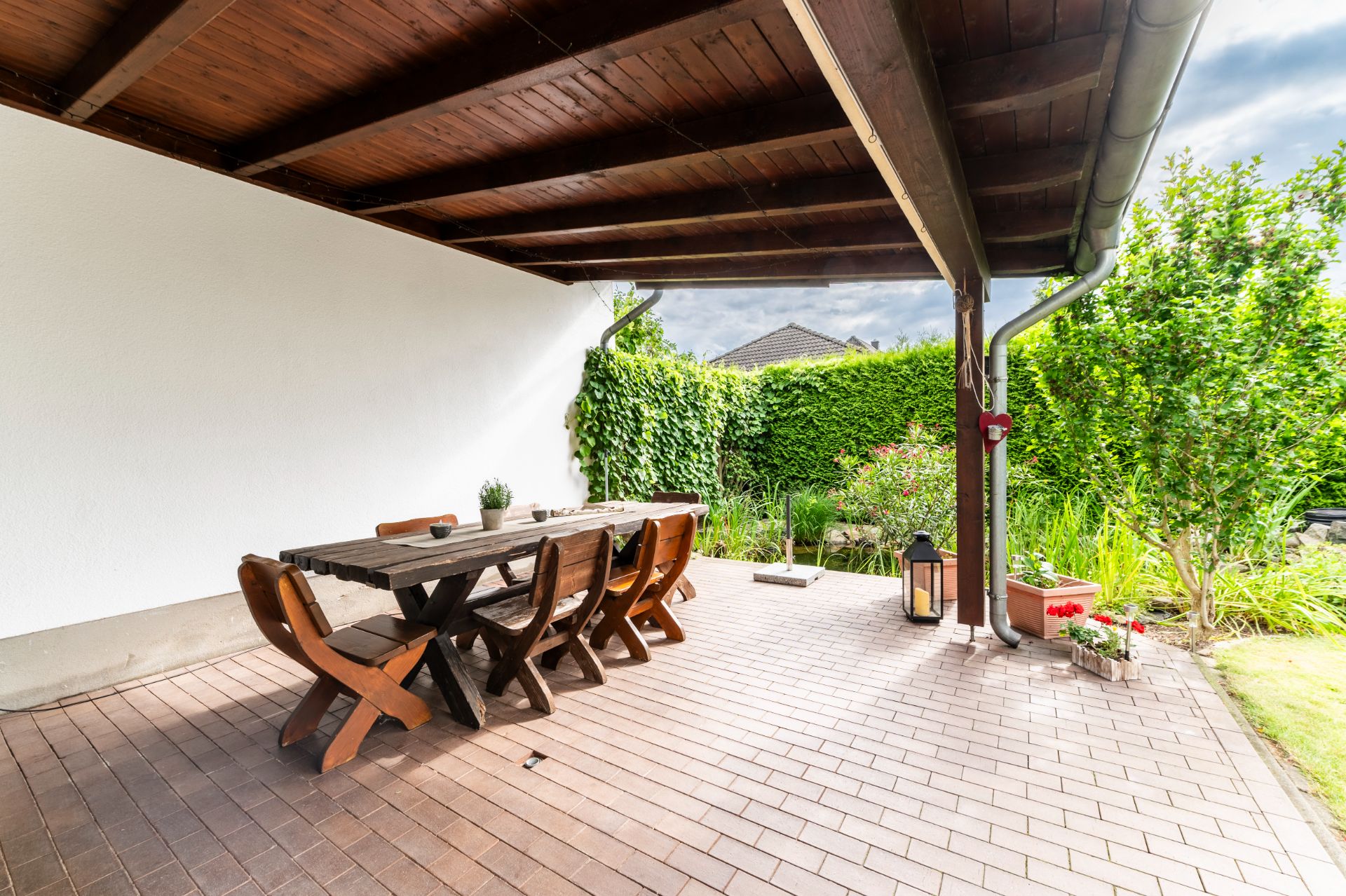Überdachte Terrasse mit Holztisch, sechs Stühlen und Blick auf Garten mit viel Grün.